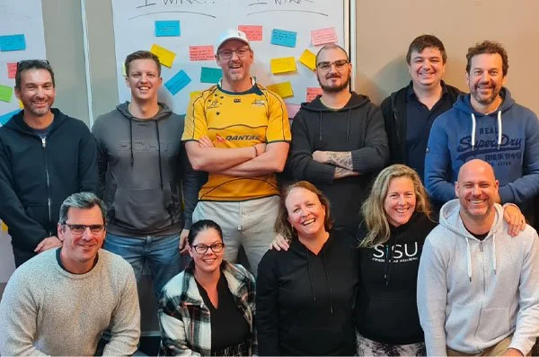 Group of 10 people posing for a photo in front of a whiteboard with colorful sticky notes.