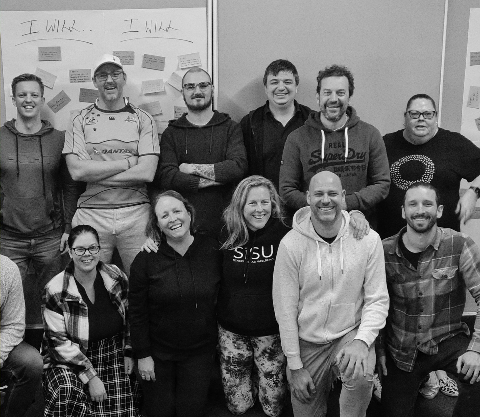 Group of smiling people at an indoor event with whiteboard in the background containing handwritten notes and papers.
