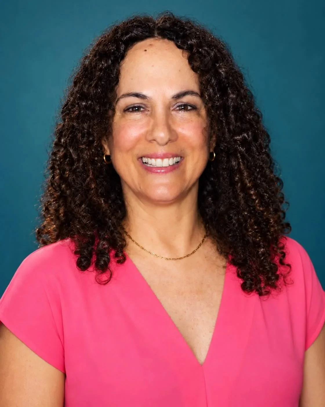 Retrato de una mujer con cabello rizado, sonrisa y camiseta rosa, fondo azul.