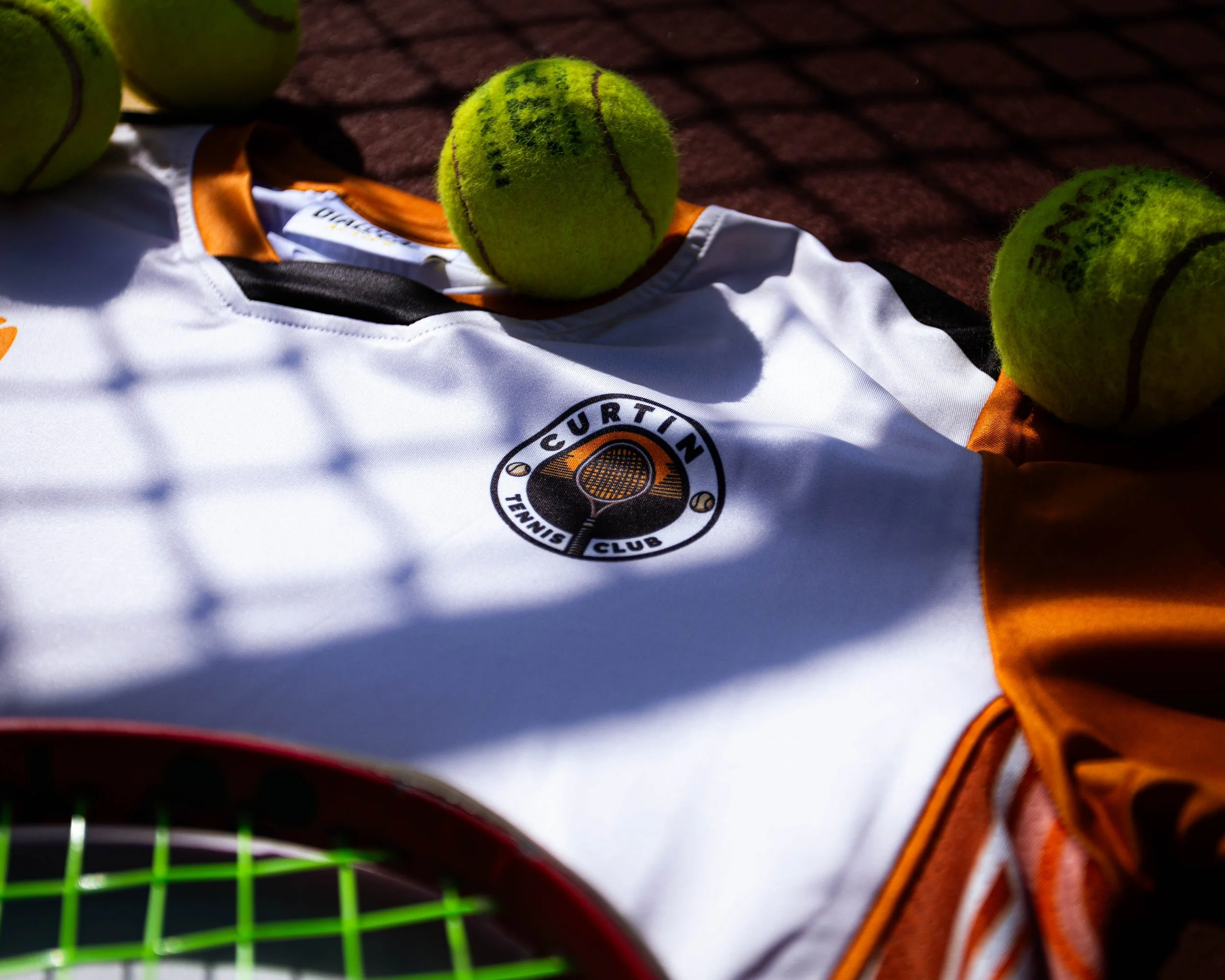 Close-up of tennis balls on a tennis court near a tennis racket and a sports jersey.