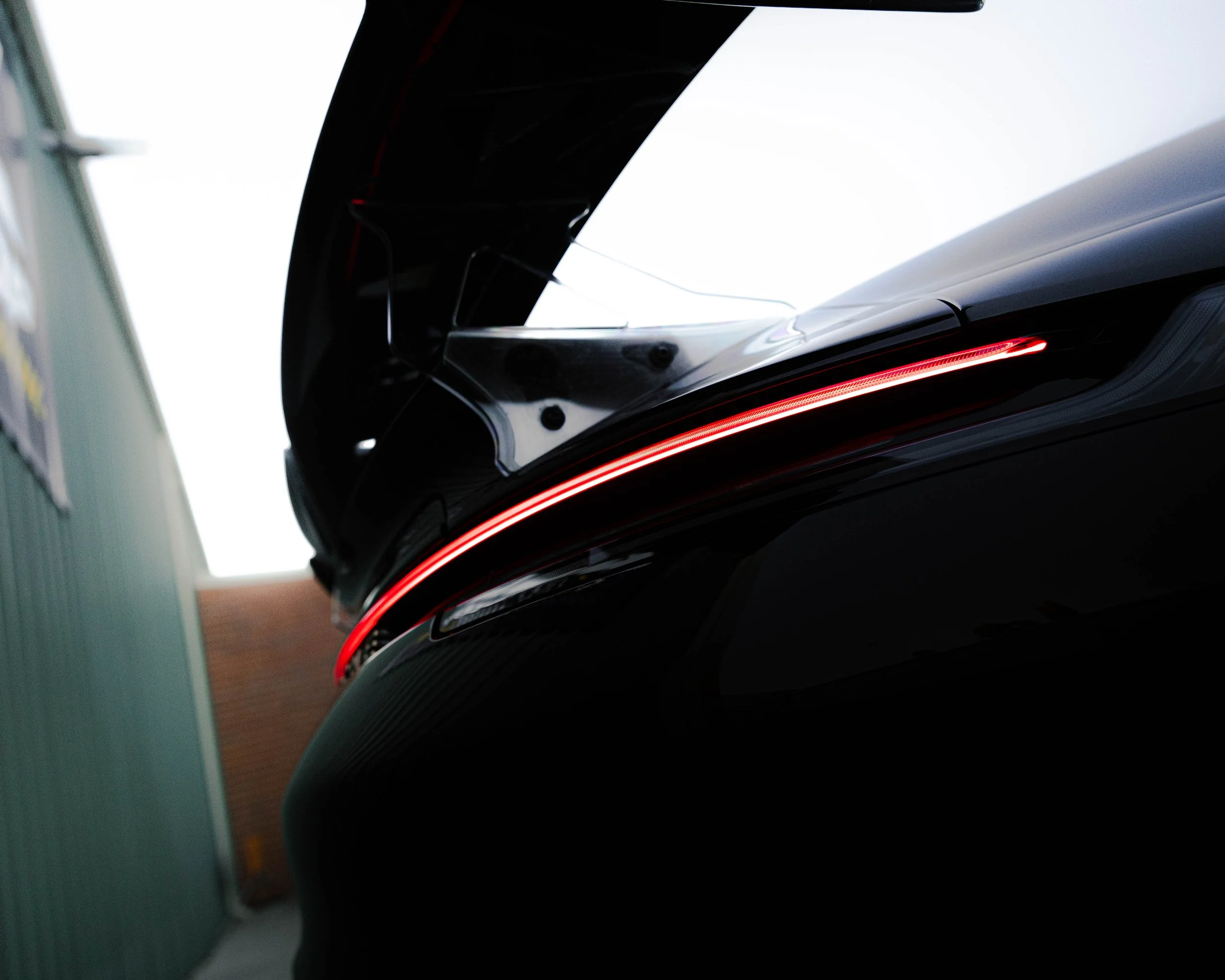 Close-up of a black object with a red illuminated strip, possibly part of a device or machinery, with a white background and blurred elements on the sides.