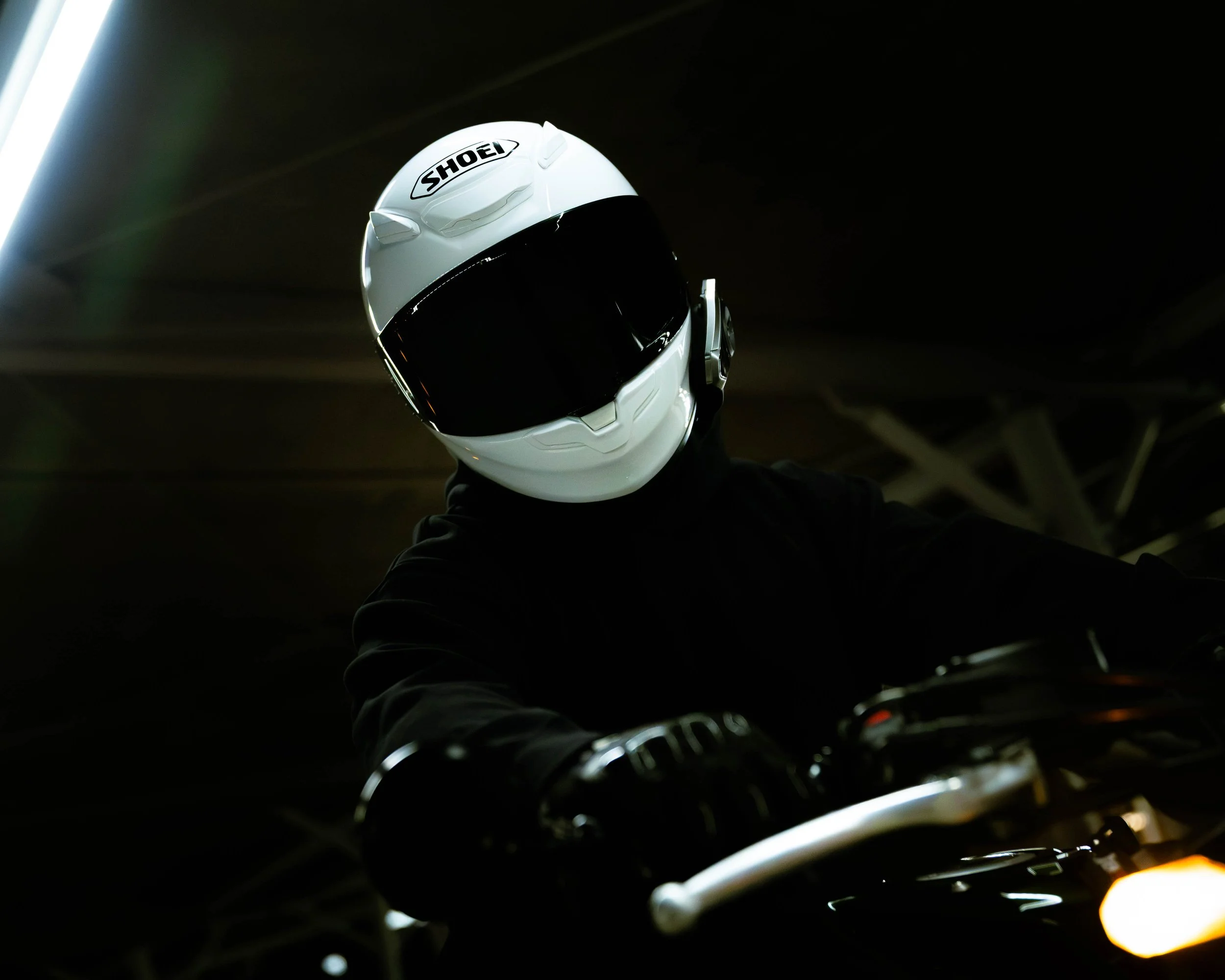 A person wearing a white Shoei motorcycle helmet with a black visor, seen from below in a dimly lit parking garage.