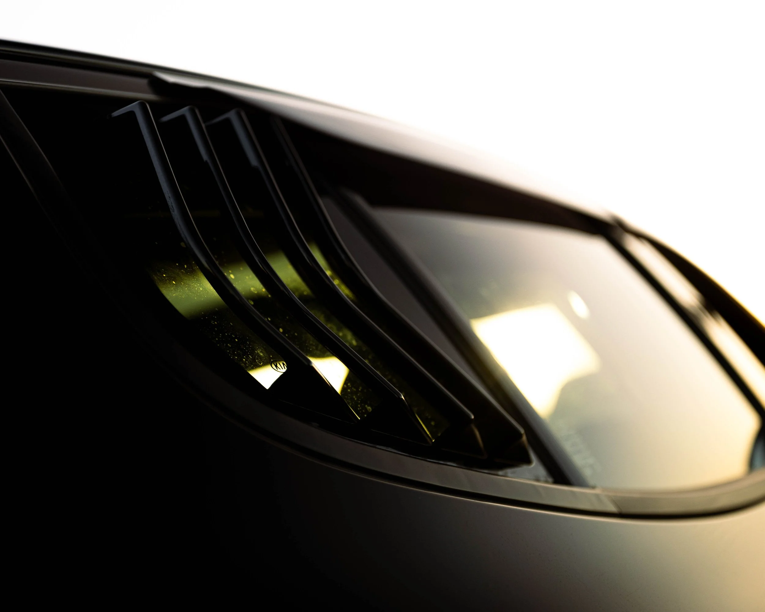 Close-up of a black car's front grille and headlight, with a white background.