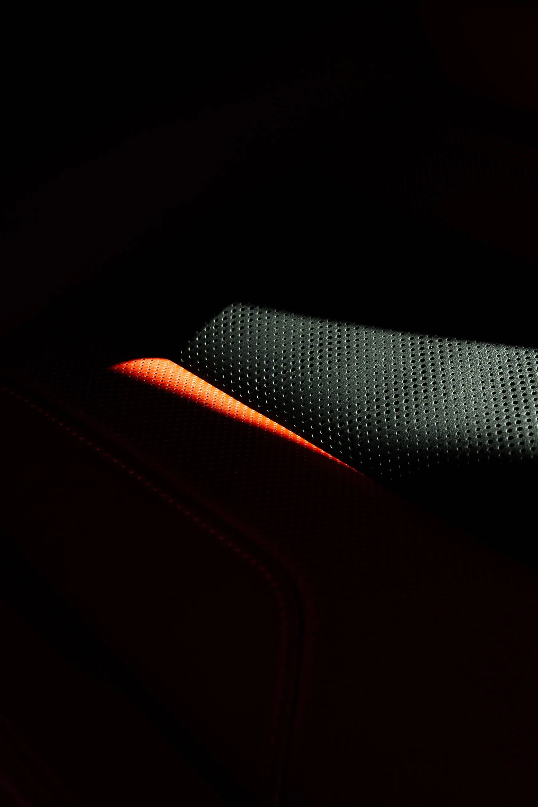 Close-up of a black electronic device with a perforated metal surface illuminated by a faint orange and white light.