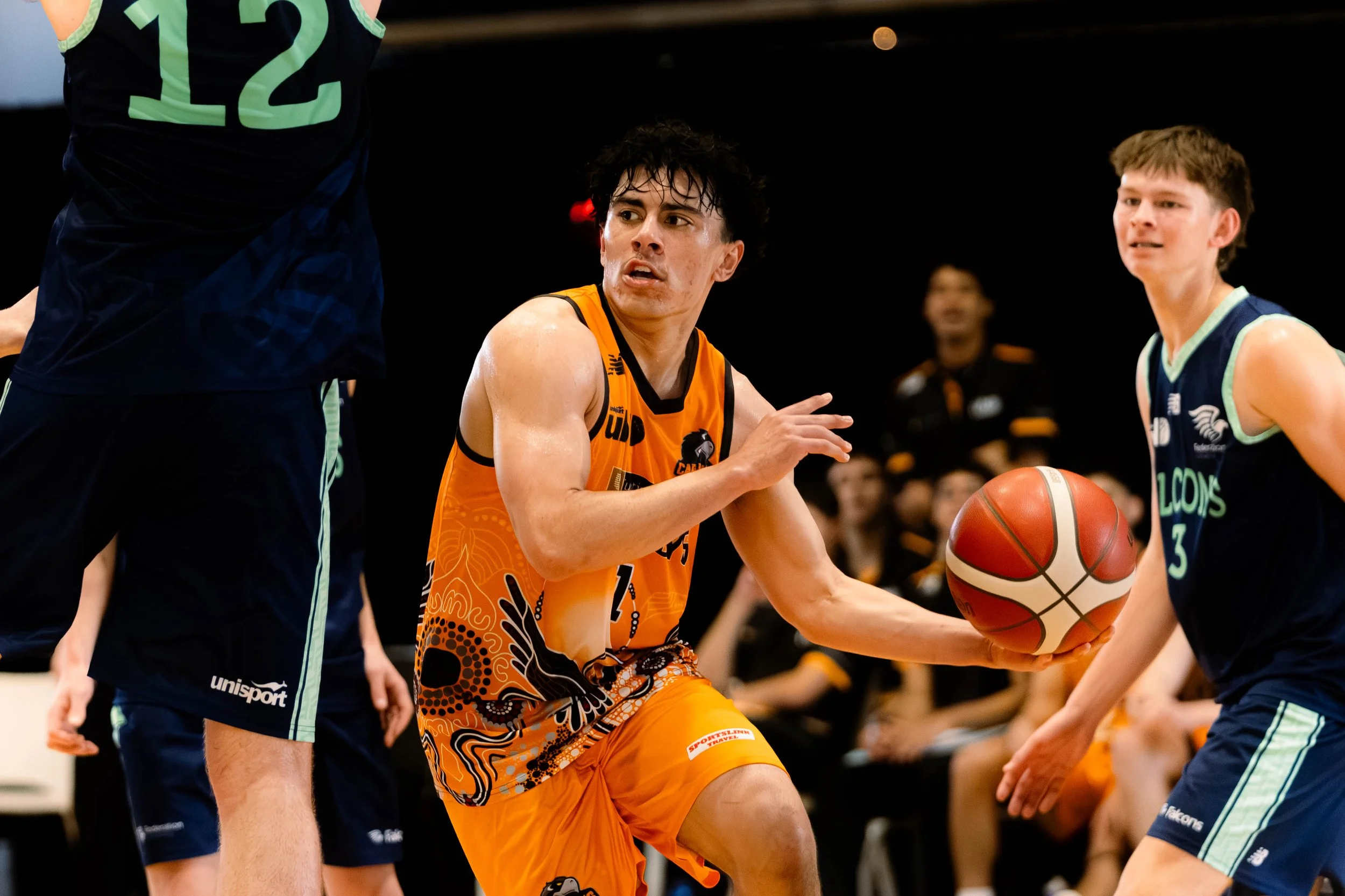 A basketball game featuring players in orange and blue uniforms battling for possession of the ball.