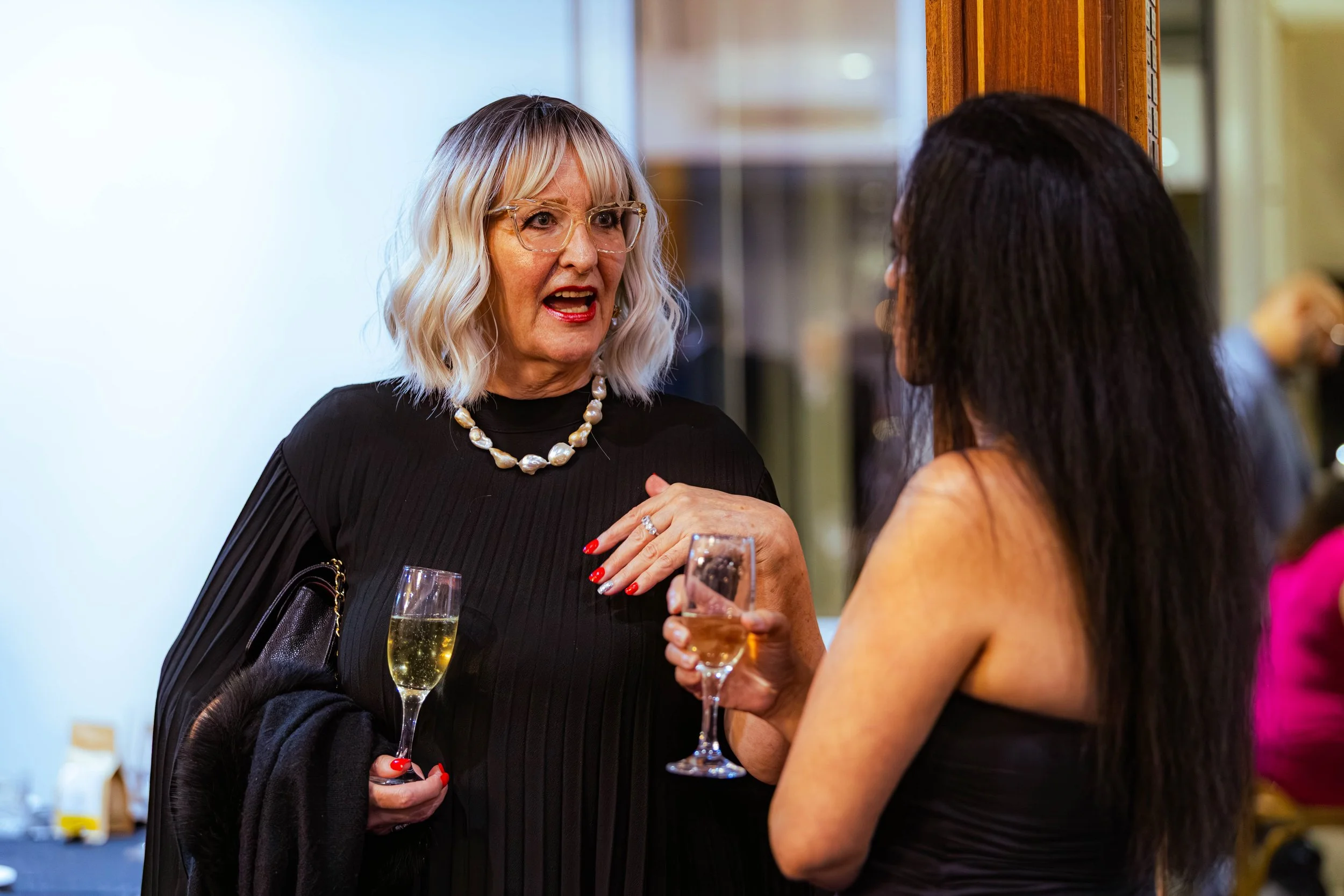 Two women having a conversation at a social event, each holding a glass of champagne.