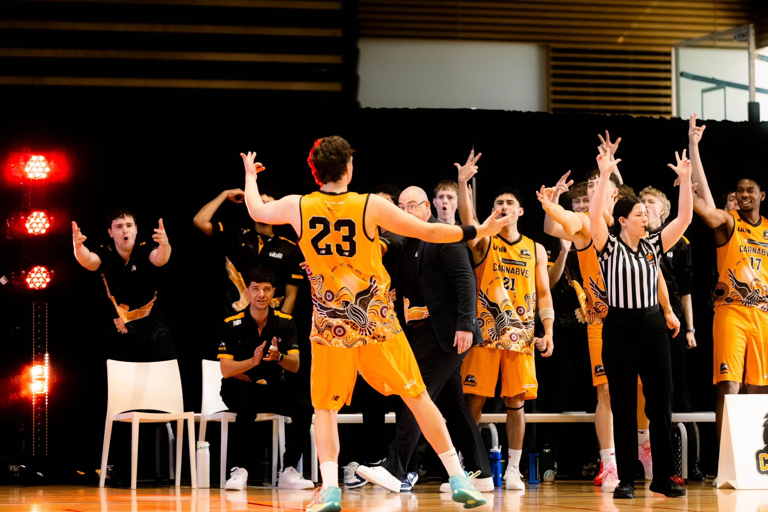 A basketball team on the court celebrating after a game, with players in yellow and black jerseys and a referee.