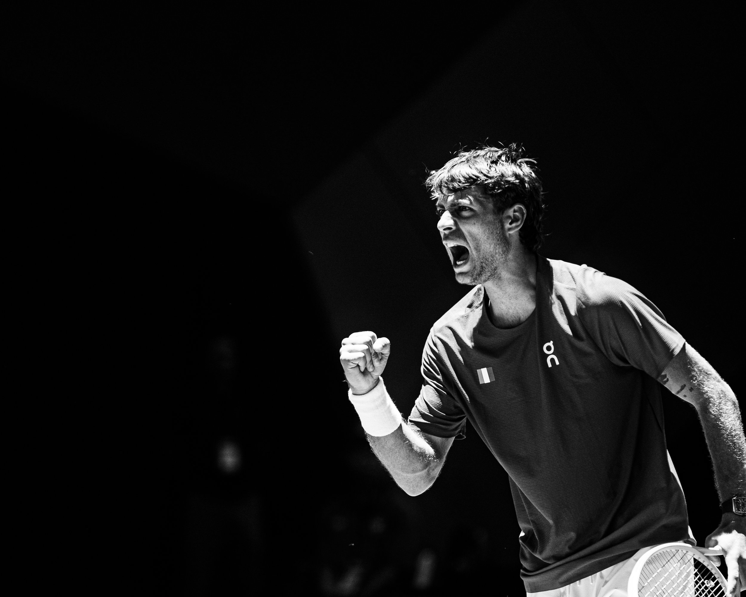 A man celebrating with a clenched fist, wearing a sports jacket, on a tennis court, with a tennis racket on the ground nearby.