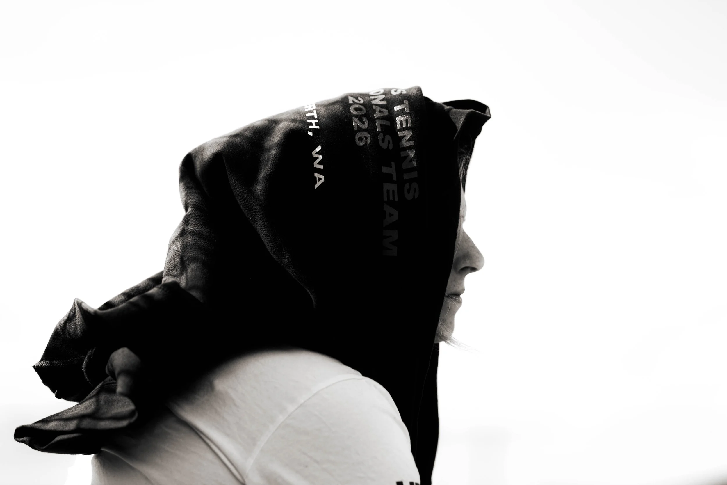A person wearing a black hoodie with white text on the hood, looking off to the side, against a plain white background.