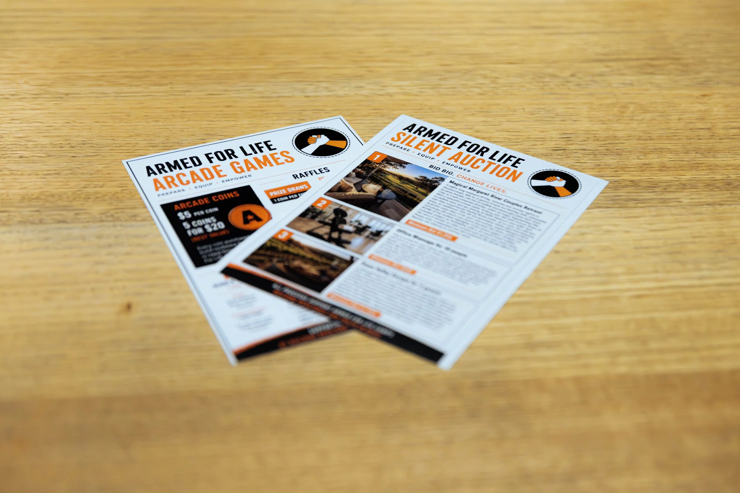 Flyers on a wooden surface promoting arcade games and a silent auction, with black, white, and orange color scheme.