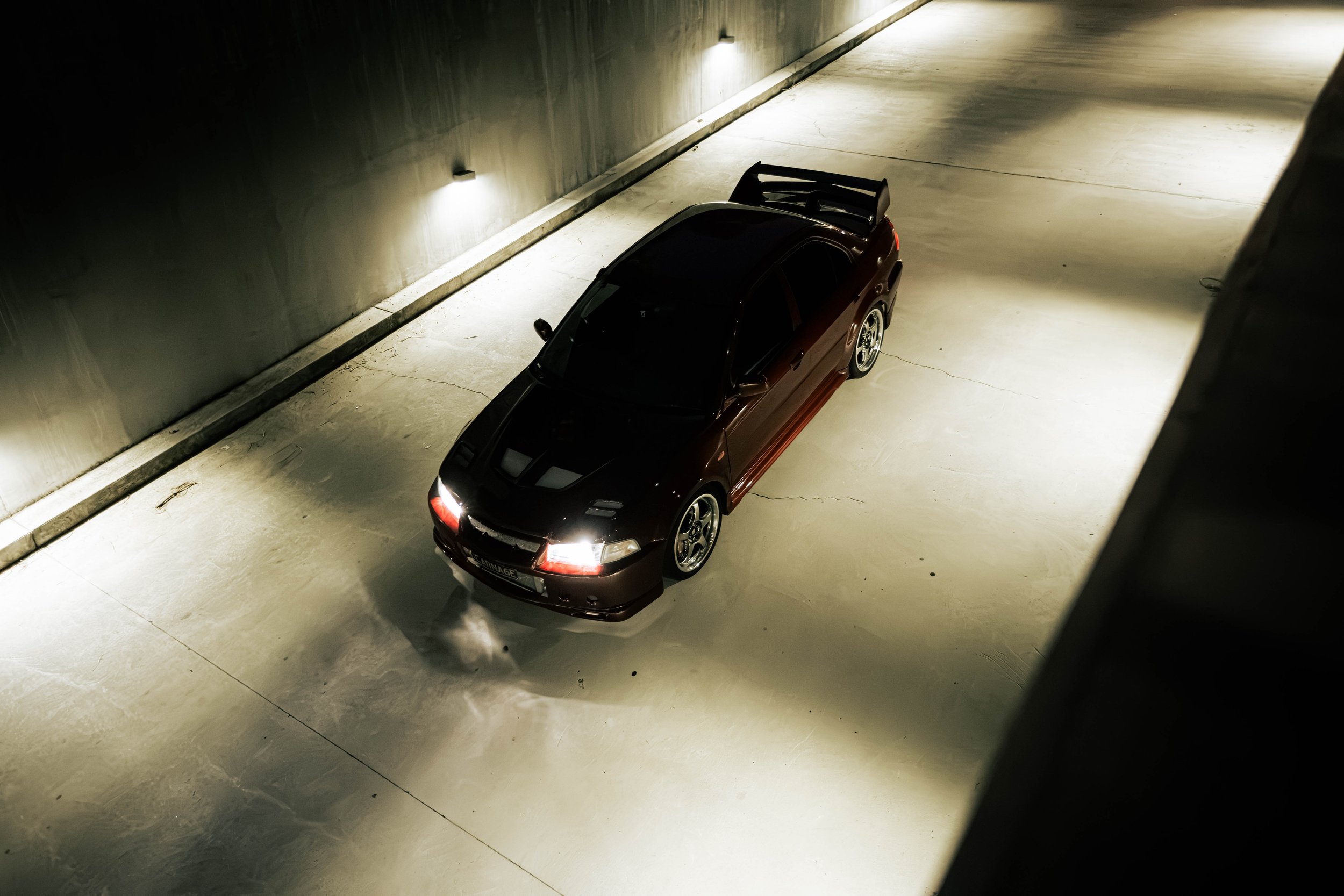 A dark-colored sports car parked in an underground parking garage with dim lighting.