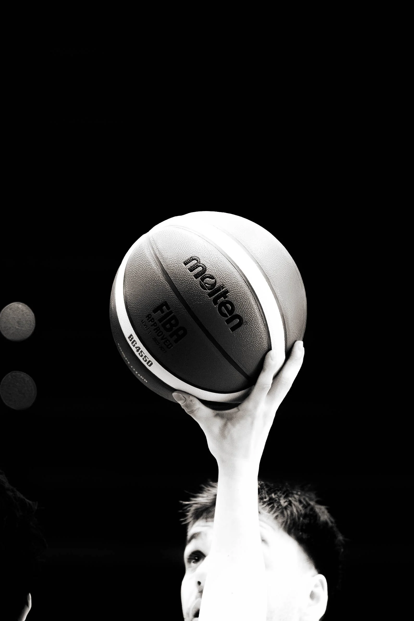 Black and white artistic photo of a child's face with an arm extended upward, holding a football, against a dark background. The football is labeled 'Sports Team'.