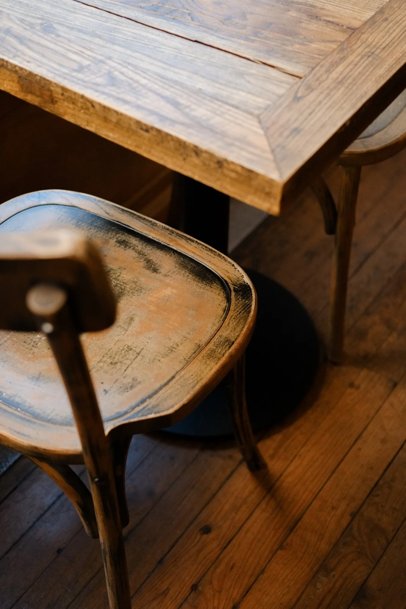 Une table en bois naturel vintage et une chaise en bois vintage, détails visibles des surfaces usées et vieilles, dans un environnement intérieur avec un plancher en bois.