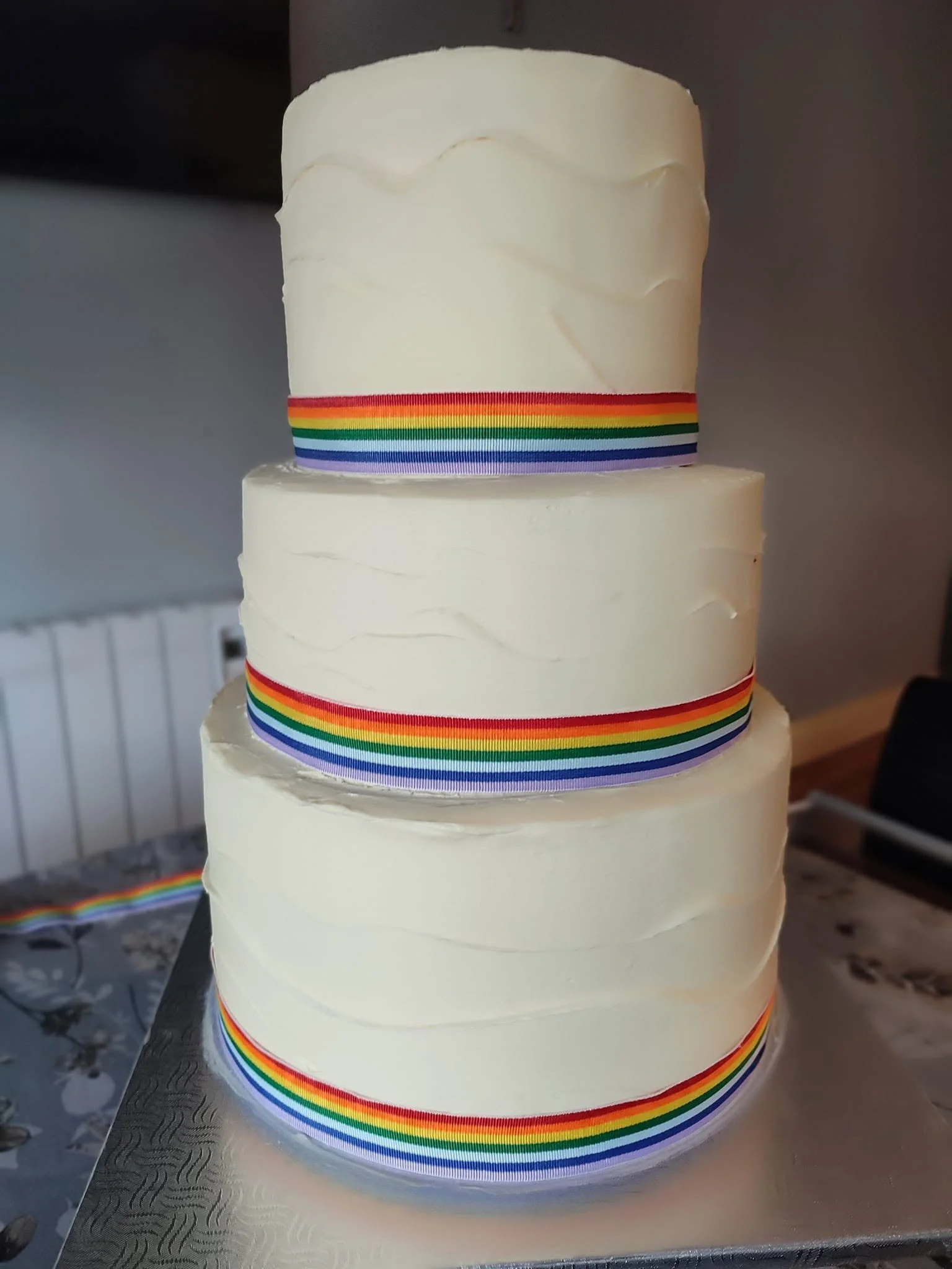 3-Layer wedding cake with white buttercream and rainbow stripes at the bottom of each layer.