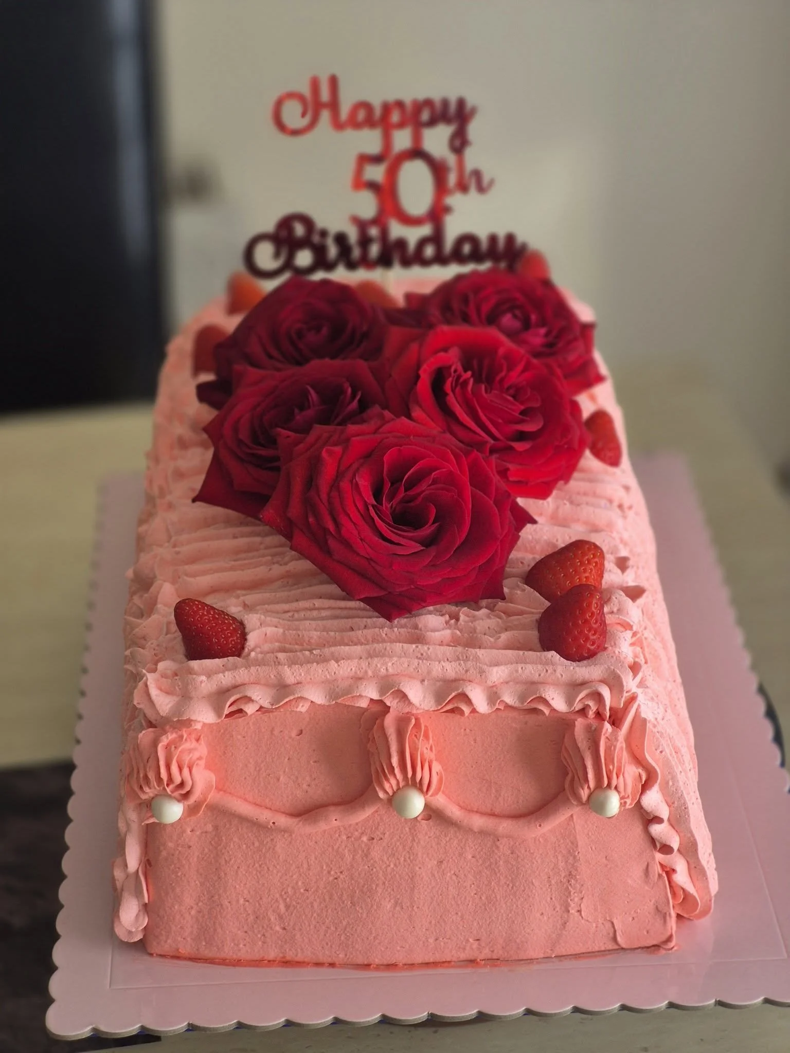 large rectangle shaped birthday cake with pink buttercream and icing and decorated with red roses.