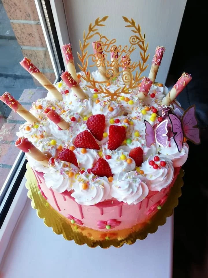 medium sized birthday cake with pink buttercream and white icing, decorated with many complimentary sweets.