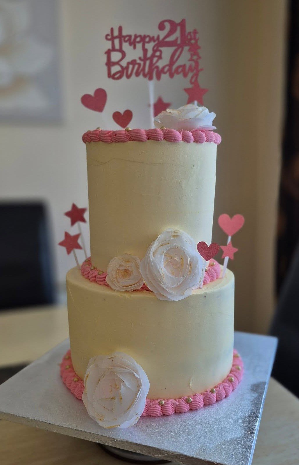 2-layer birthday cake with white buttercream and pink icing at the edges with a floral design.