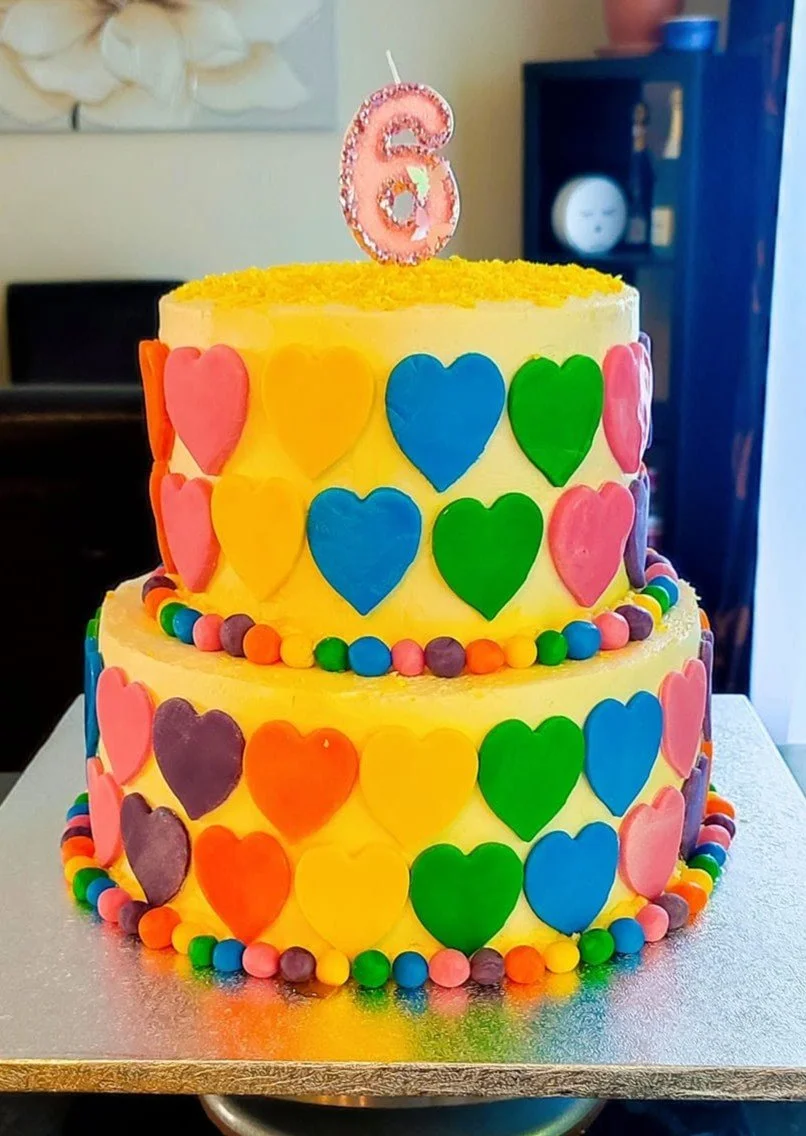 2-Layer birthday cake with yellow butter cream and rainbow hearts and spheres made out of fondant.