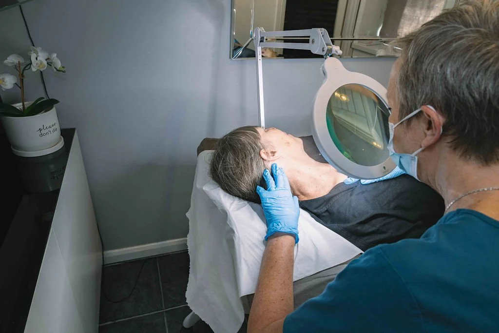 Sarah Hurst assessing a client’s skin under a magnifying lamp at her Brighton clinic.