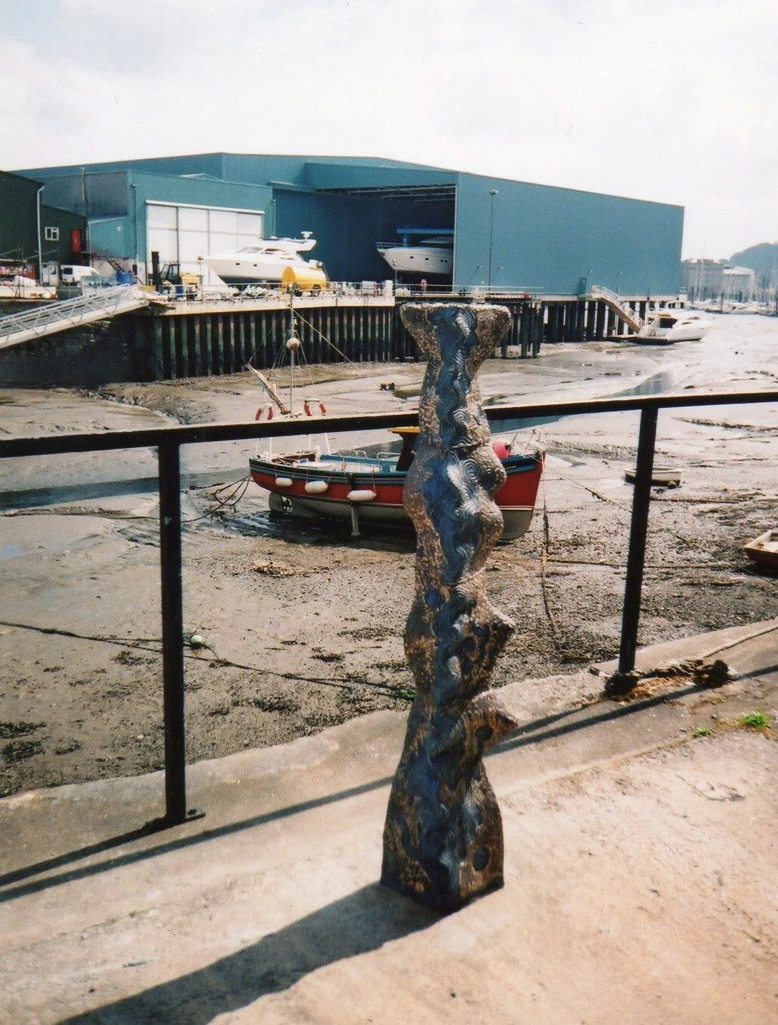 Marina with boats, a blue storage building, and a tall decorative ceramic sculpture in the foreground.