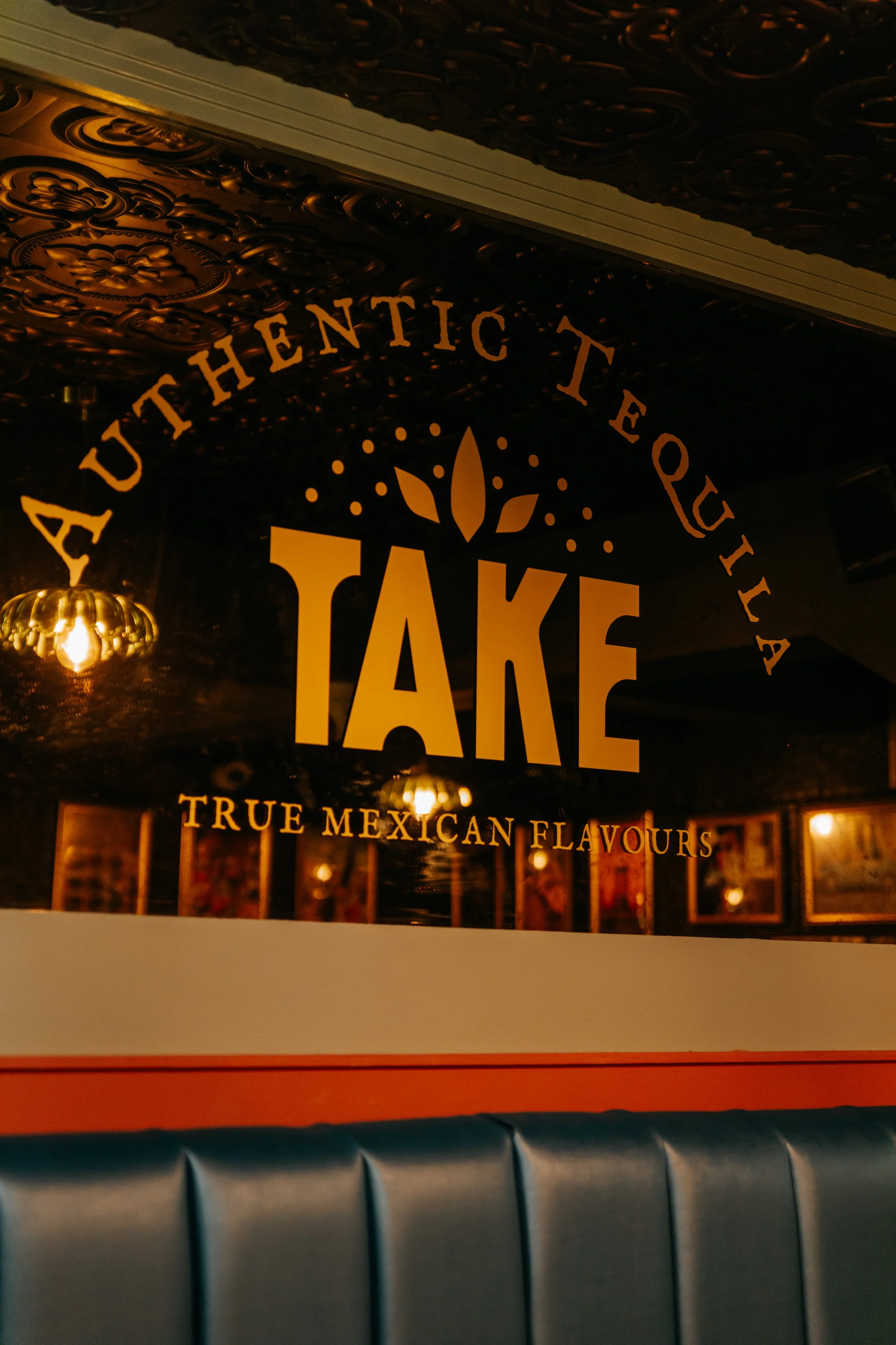 A sign with the words 'Authentic Tequila' and 'True Mexican Flavours' displayed on a dark ornate wall, with warm lighting reflecting off the surface.