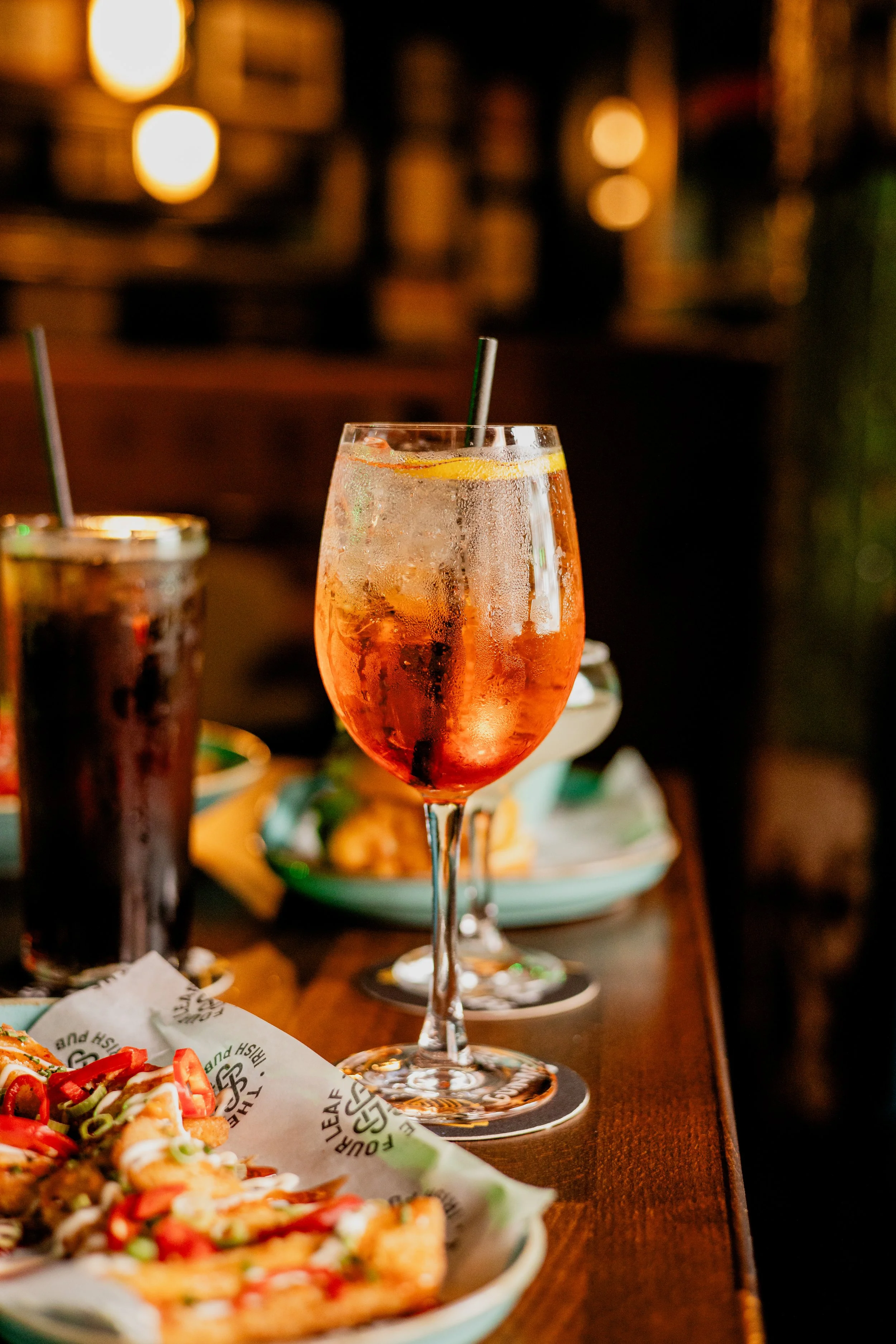 A glass of pink cocktail with lemon slice and straw on a wooden table, blurred background