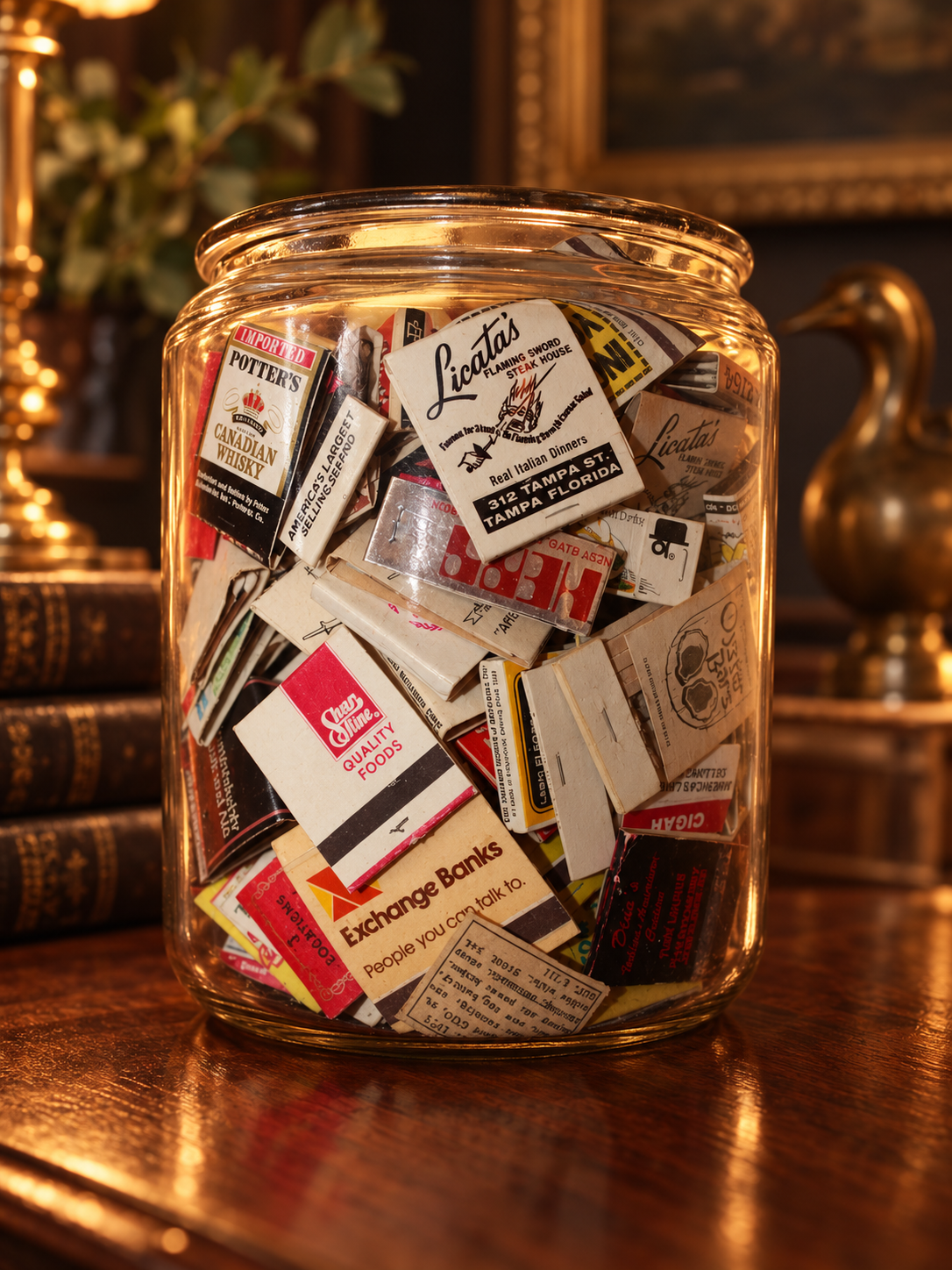 A glass jar filled with vintage matchbooks on a wooden table. The matchbooks are from various establishments, featuring different designs and text.