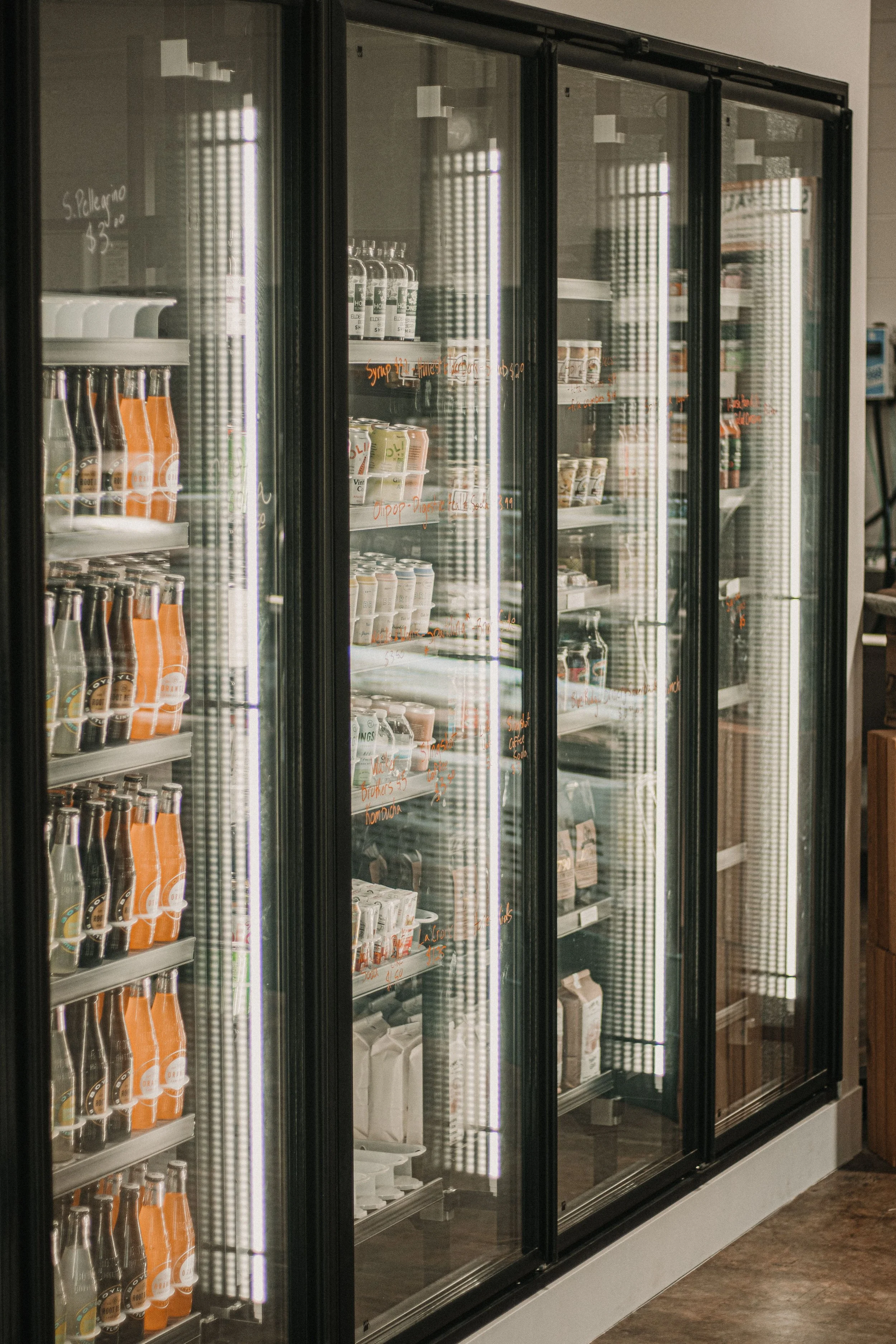 A commercial refrigerator with glass doors filled with various bottled and canned drinks, located in a store aisle.