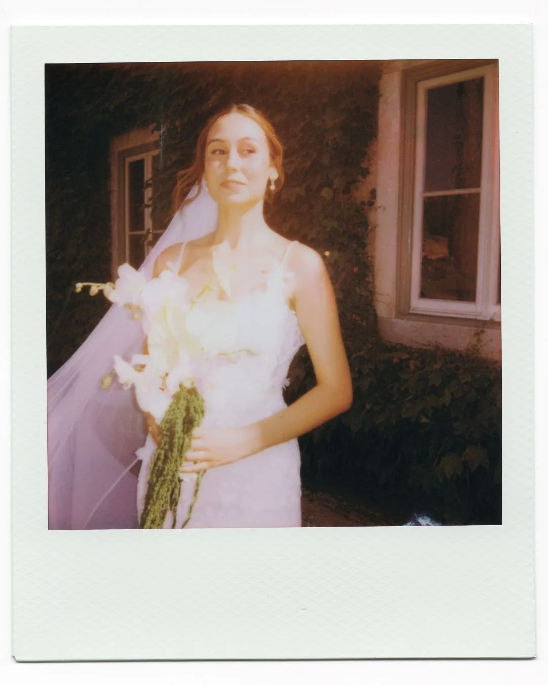 Bride in a wedding dress holding a bouquet of flowers, posing outdoors at night with illuminated windows in the background, photographed at a wedding in Portugal.