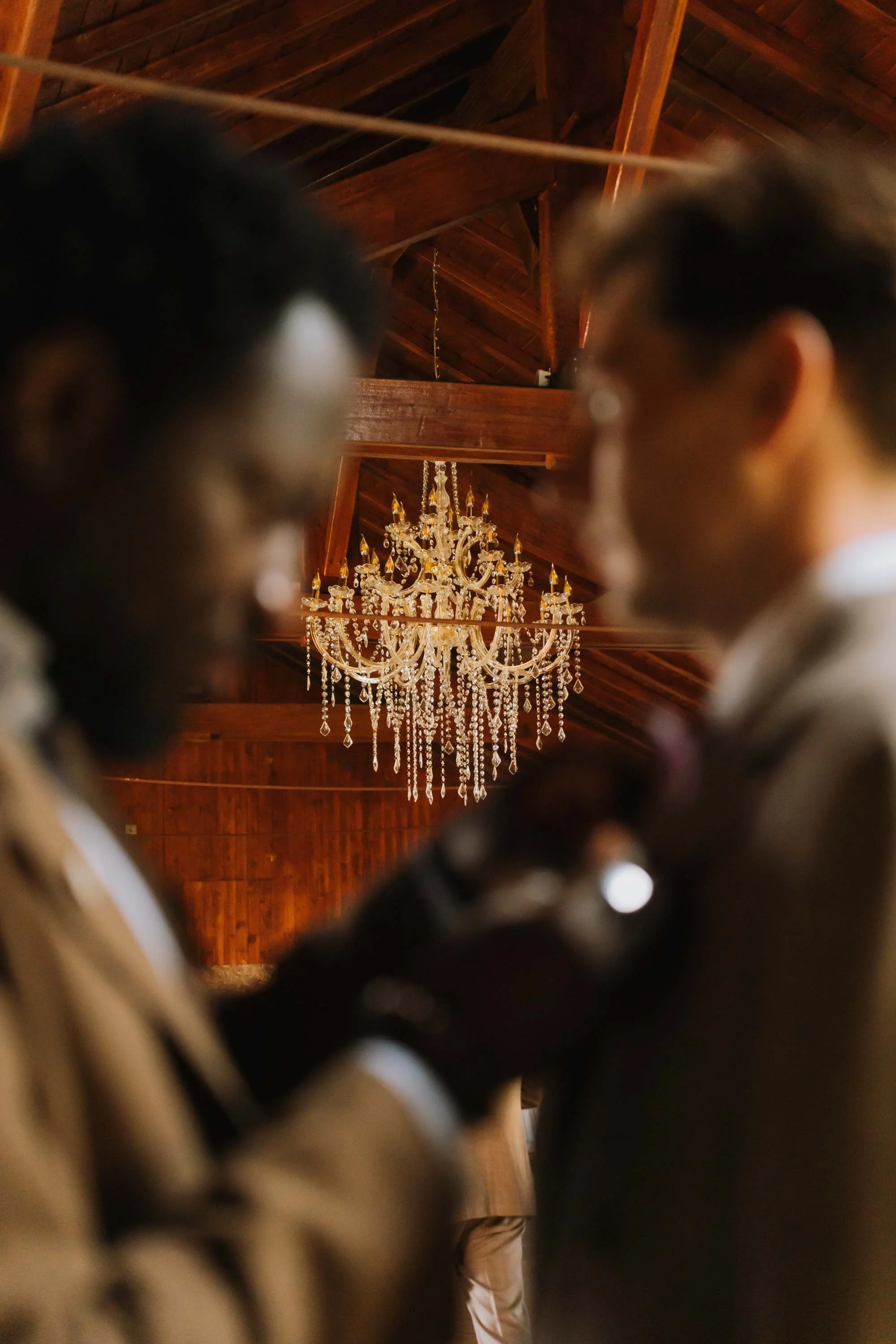 People at a wedding ceremony, photographed from above, with a crystal chandelier and wooden ceiling in the background, photographed at a wedding in Portugal.