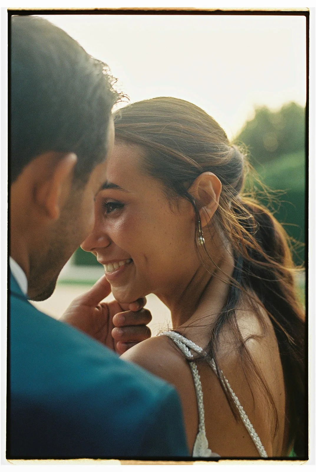 Couple sharing a tender moment outdoors at sunset, with the bride smiling and closing her eyes as the groom gently touches her chin, photographed at a wedding in Portugal.