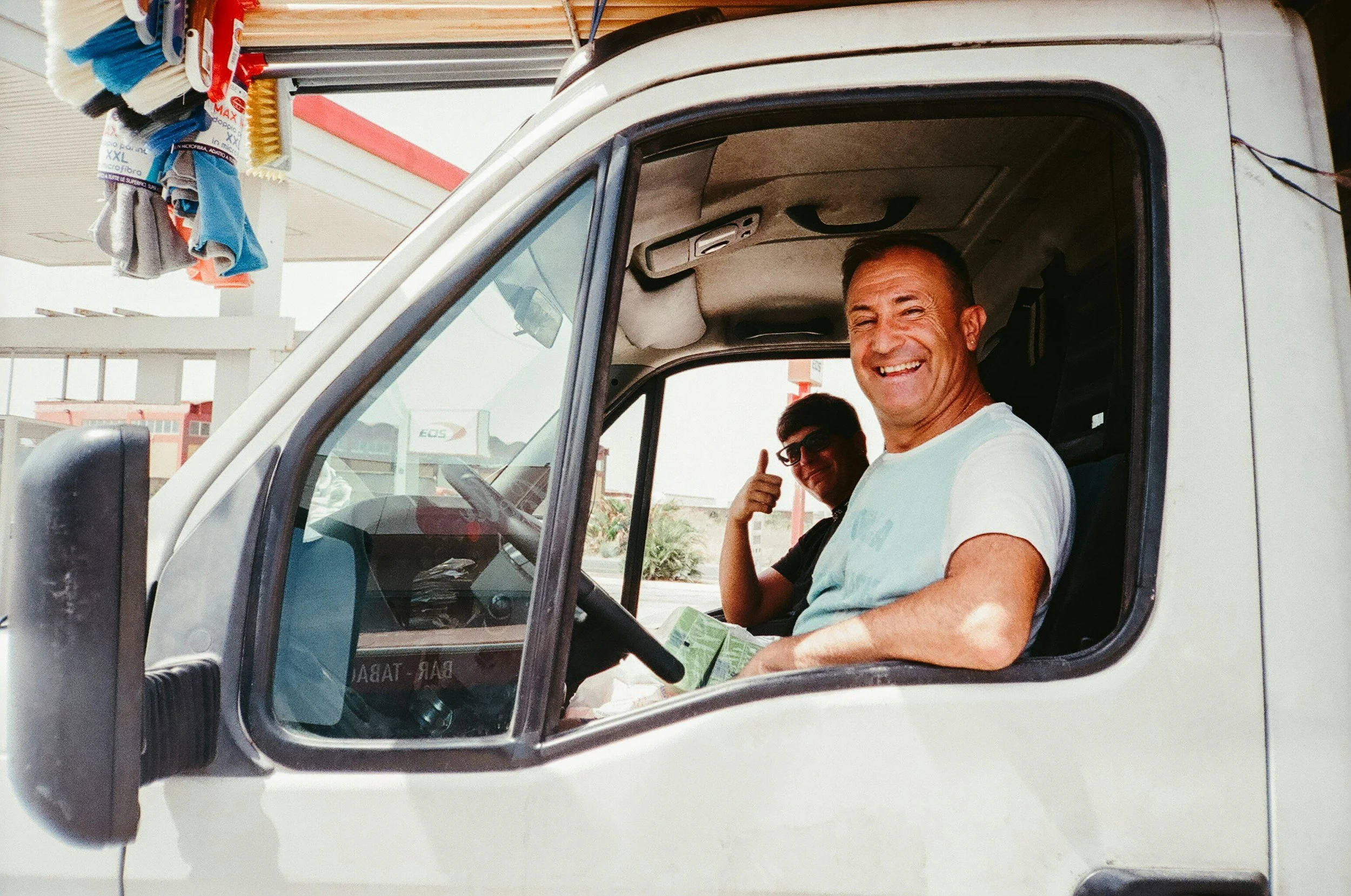 Two men sitting inside a white delivery truck, smiling and giving thumbs-up signs.