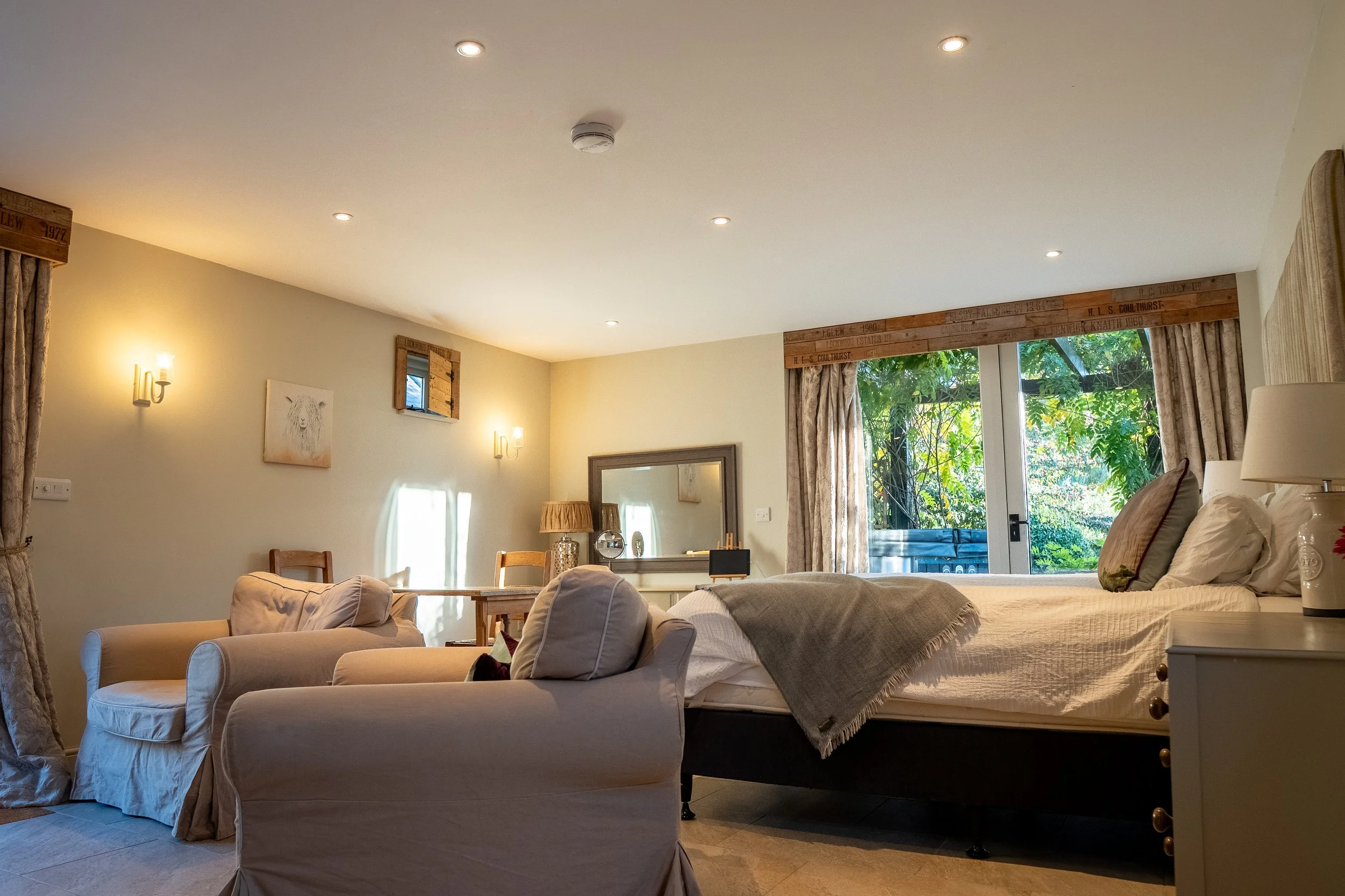 The Garden Room with 2 armchairs, a super king bed and patio windows overlooking the hot tub on the patio
