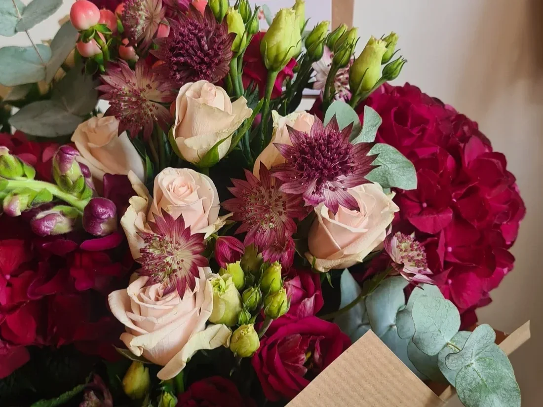 A colorful bouquet of various flowers including pink roses, deep red hydrangeas, and purple and pink astilbe, accented with eucalyptus leaves.