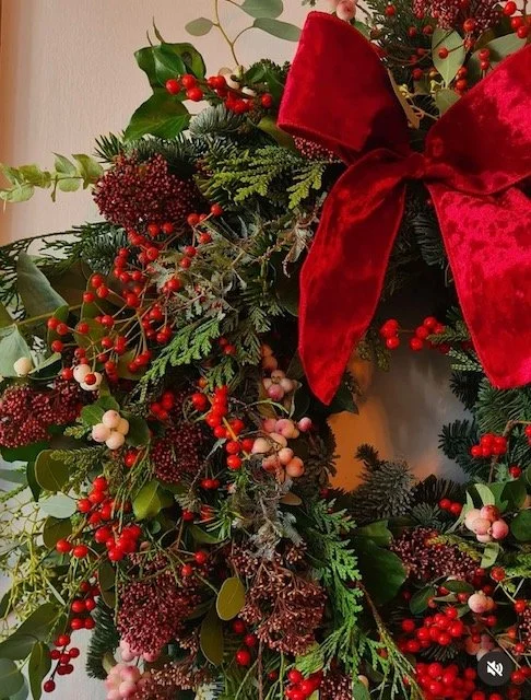 Close-up of a Christmas wreath decorated with red berries, green foliage, and a large red velvet bow.