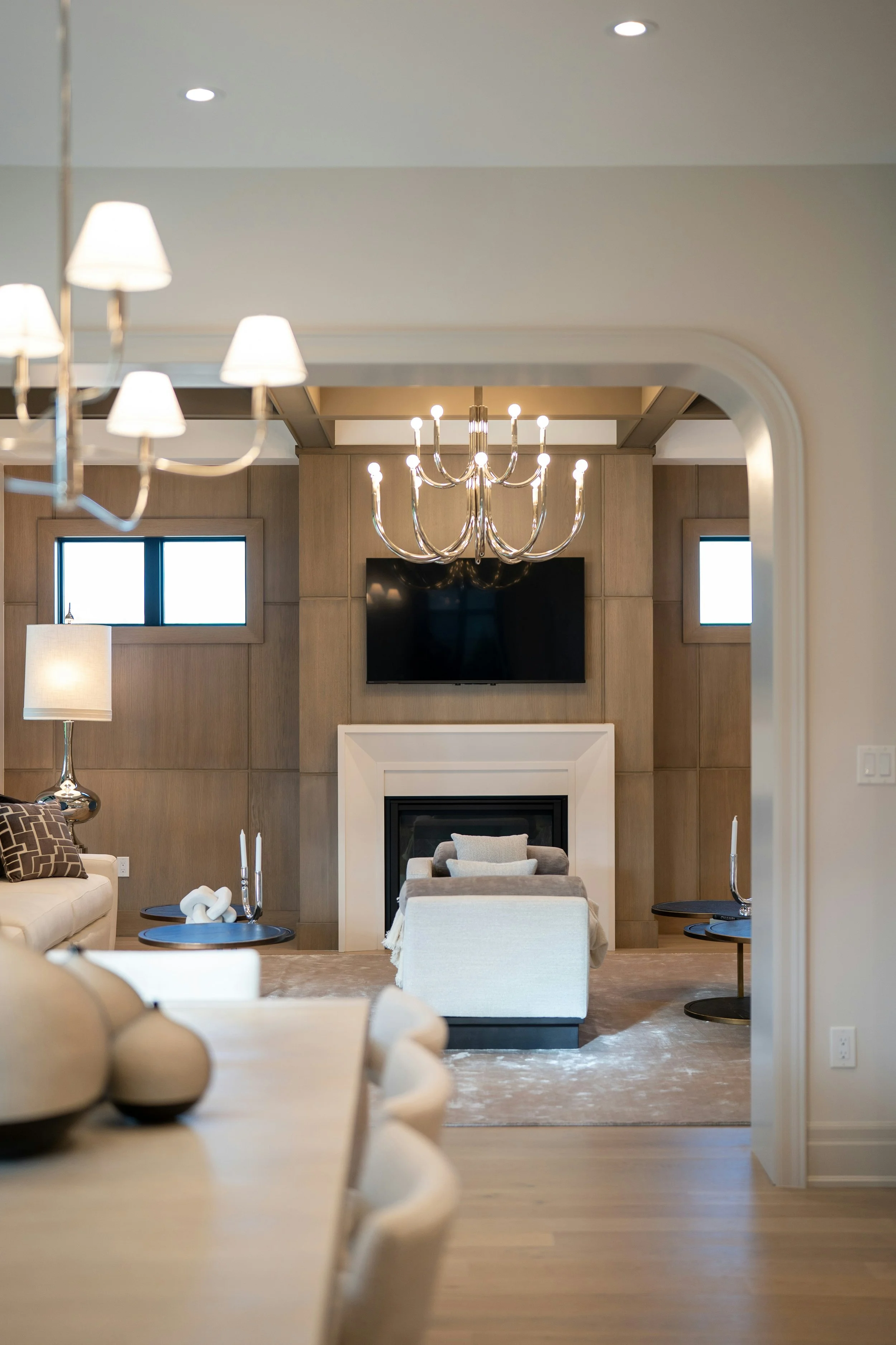 Interior living room with chandelier, wall-mounted TV, fireplace, multiple windows, and contemporary furniture.