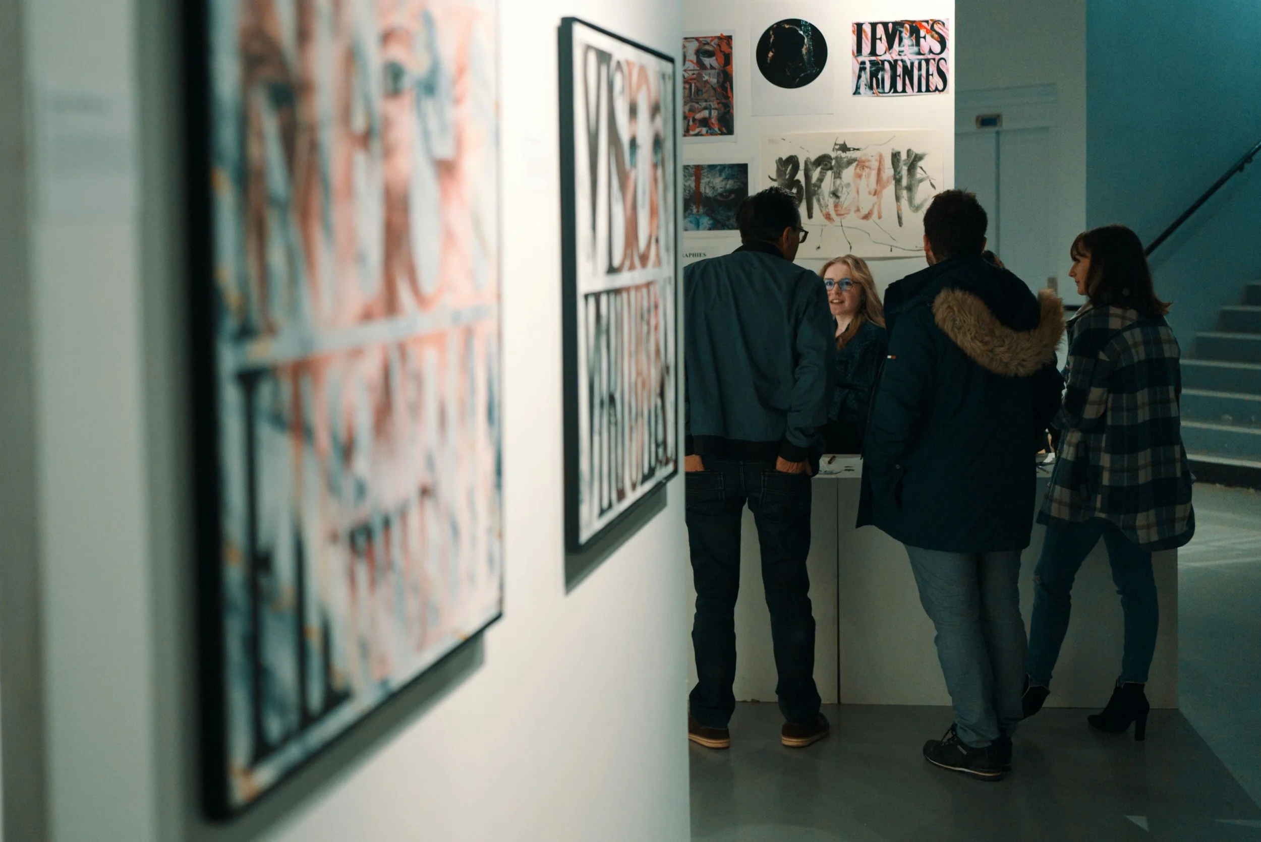 Groupe de quatre personnes discutant dans une galerie d'art, avec des œuvres colorées en arrière-plan.