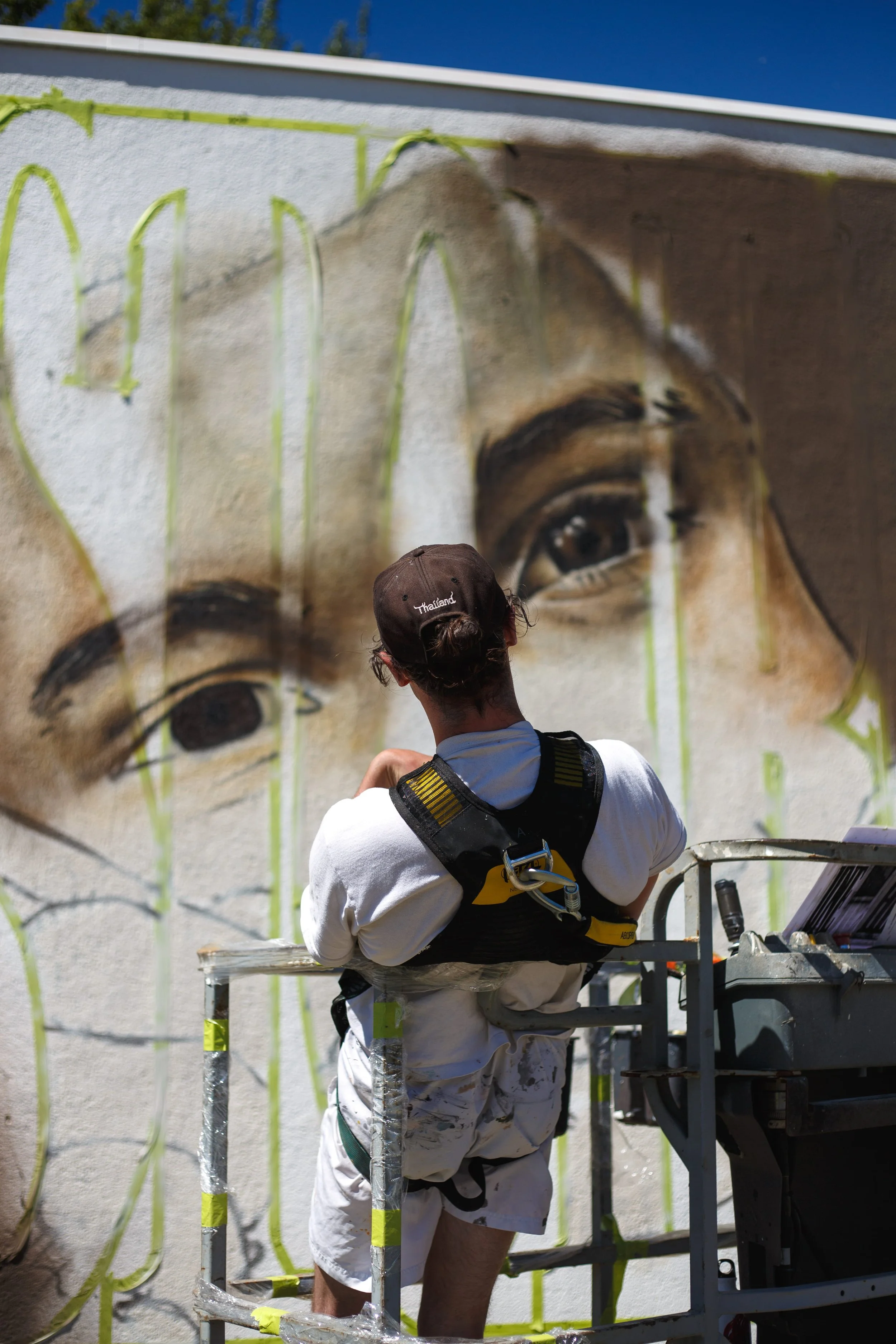Un artiste muraliste graffeur, sur la nacelle, visualisant son oeuvre sur le mur