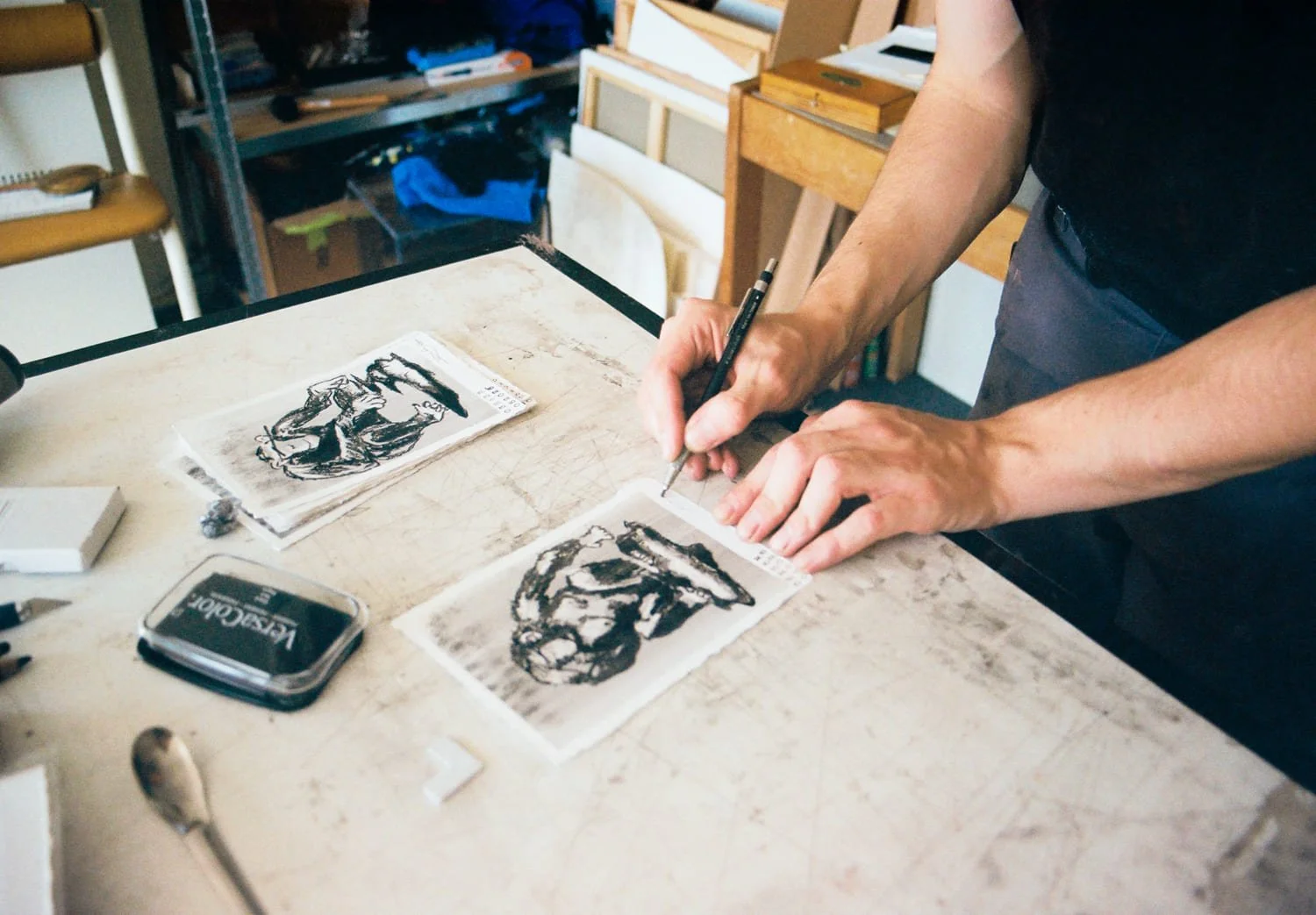 Une personne en train de créer une gravure ou une lithographie sur une plaque en utilisant un pinceau ou un outil à main, avec plusieurs plaques d'impression semblables sur la table.