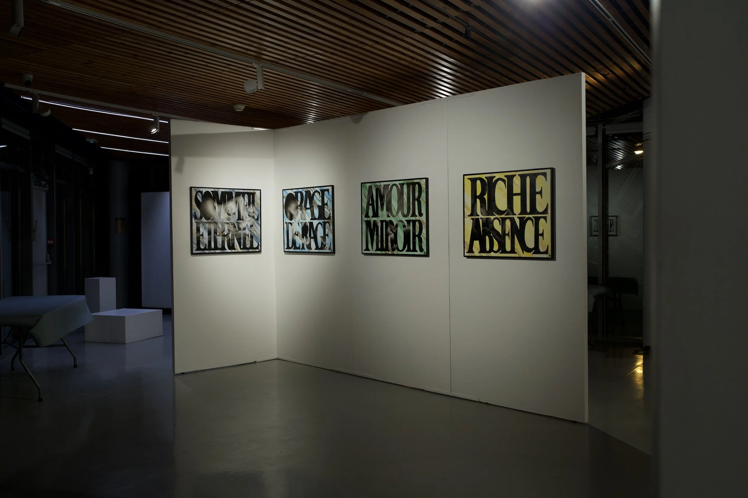 Exposition avec quatre affiches encadrées, affichant des mots en français : 'SOMMEIL', 'ESPACE', 'AMOUR', 'RÊCHE ABSENCE', dans un musée ou une galerie d'art, sous un plafond en bois, avec un espace d'exposition lumineux.