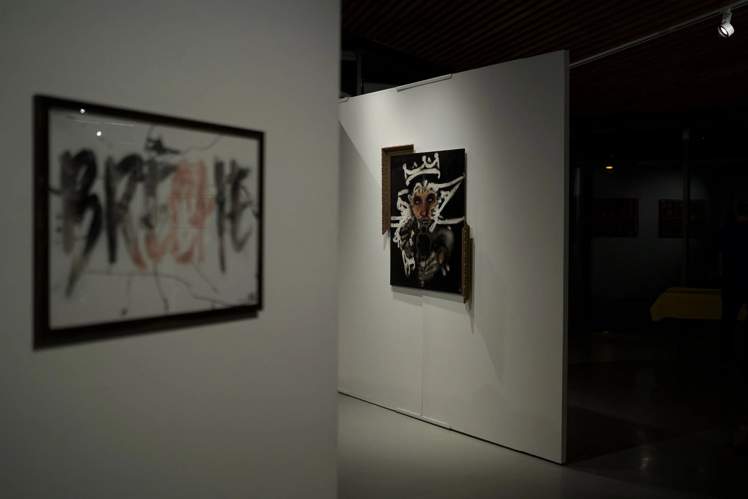 Une galerie d'art avec des œuvres accrochées sur des murs blancs, avec un éclairage ciblé sur les tableaux.