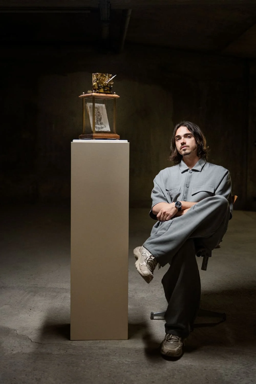 Un homme assis à côté d'une vitrine contenant un objet ancien, dans une pièce sombre.