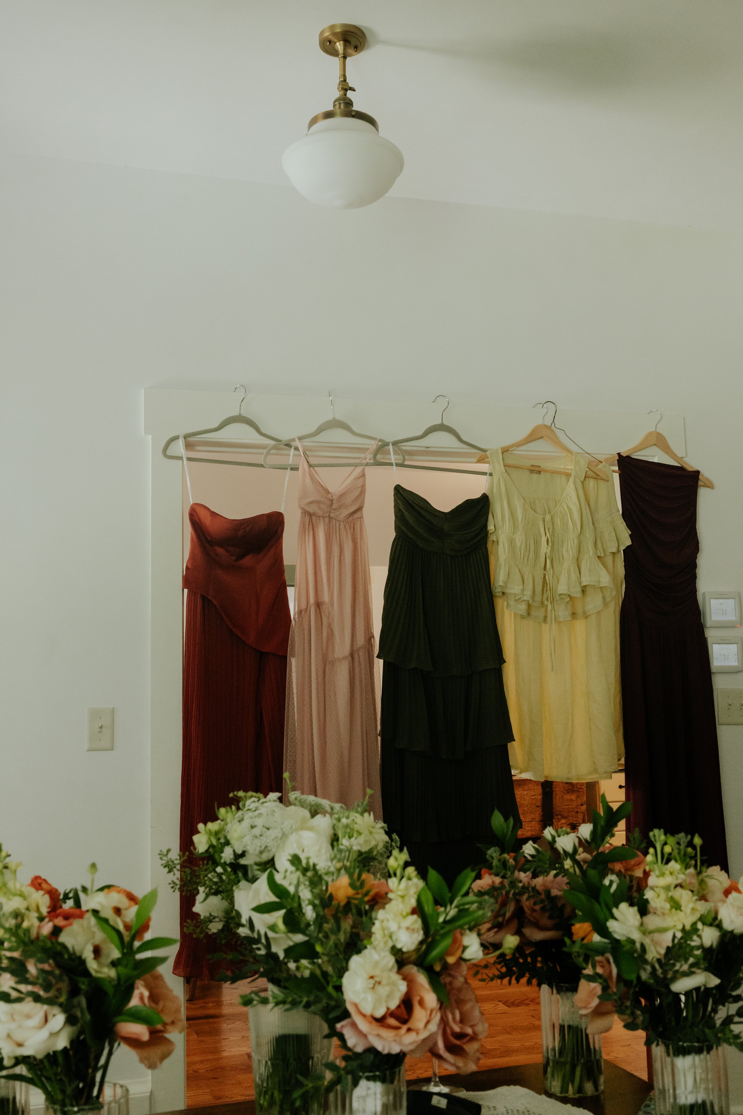Various colorful dresses hanging on a garment rack in a room decorated with flowers on a table.