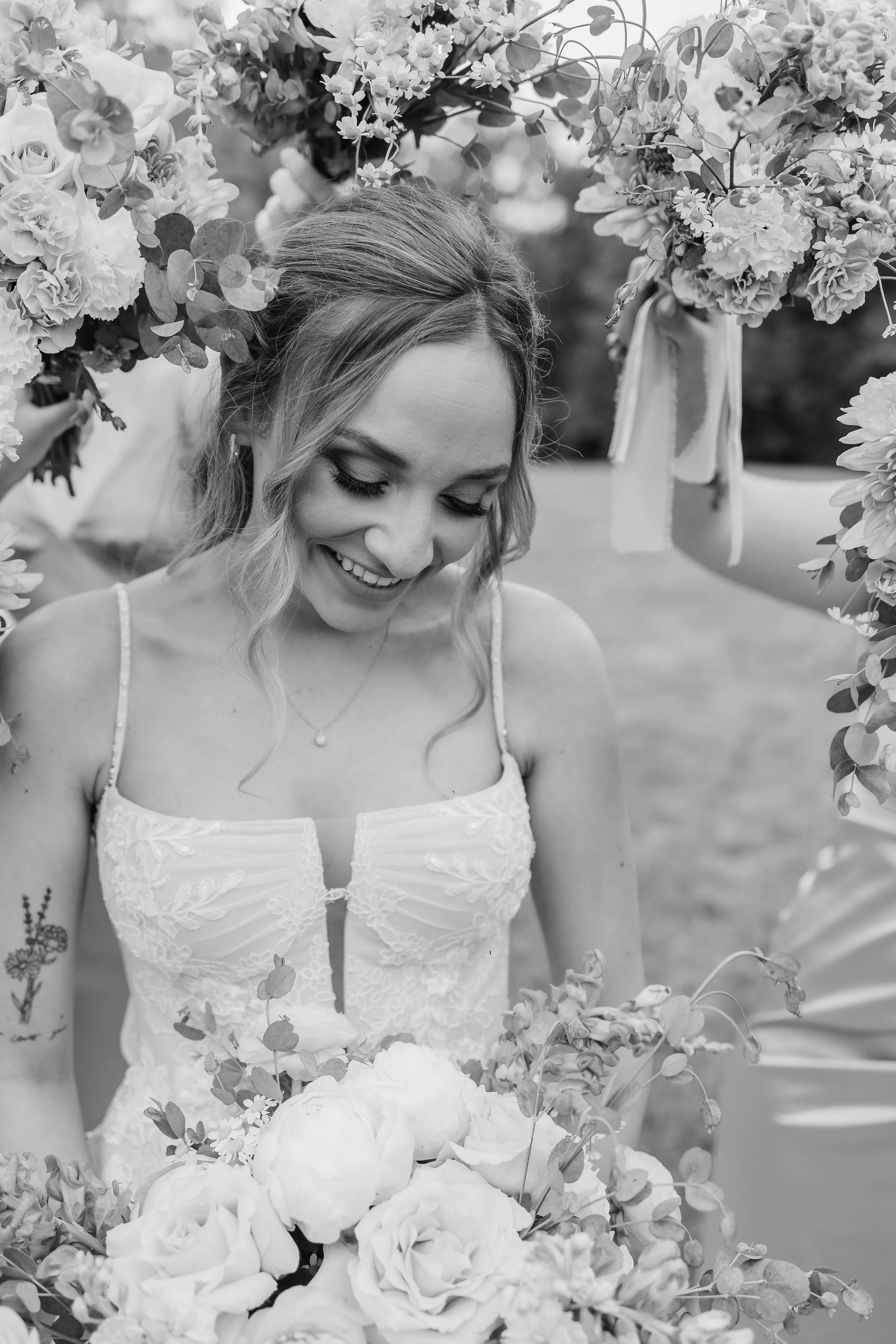A woman in a wedding dress smiling while surrounded by a floral arrangement with large flowers and greenery