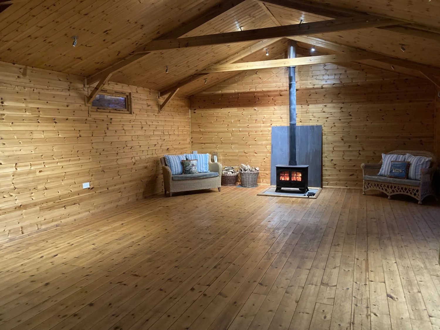 Cozy wooden room with wicker sofas, a wood-burning stove, and a rustic decor.
