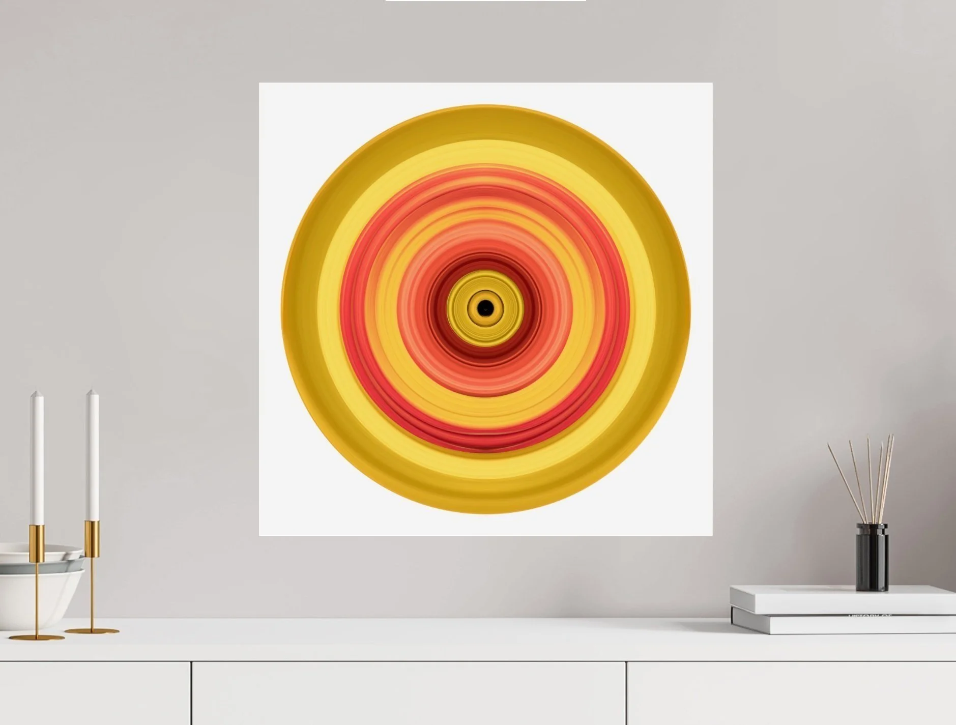 Abstract circular painting with concentric rings in orange, red, and yellow hues on a white wall, above a minimalist white tabletop with candles and books.