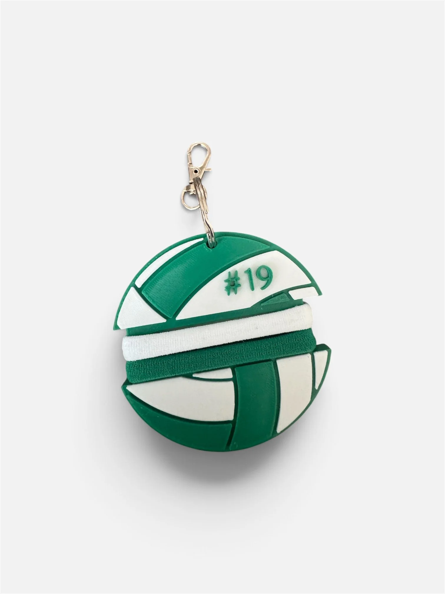 A round, green and white object resembling a simplified male genitalia, with a plastic clip attached at the top. The object has a hashtag '#19' printed on it.