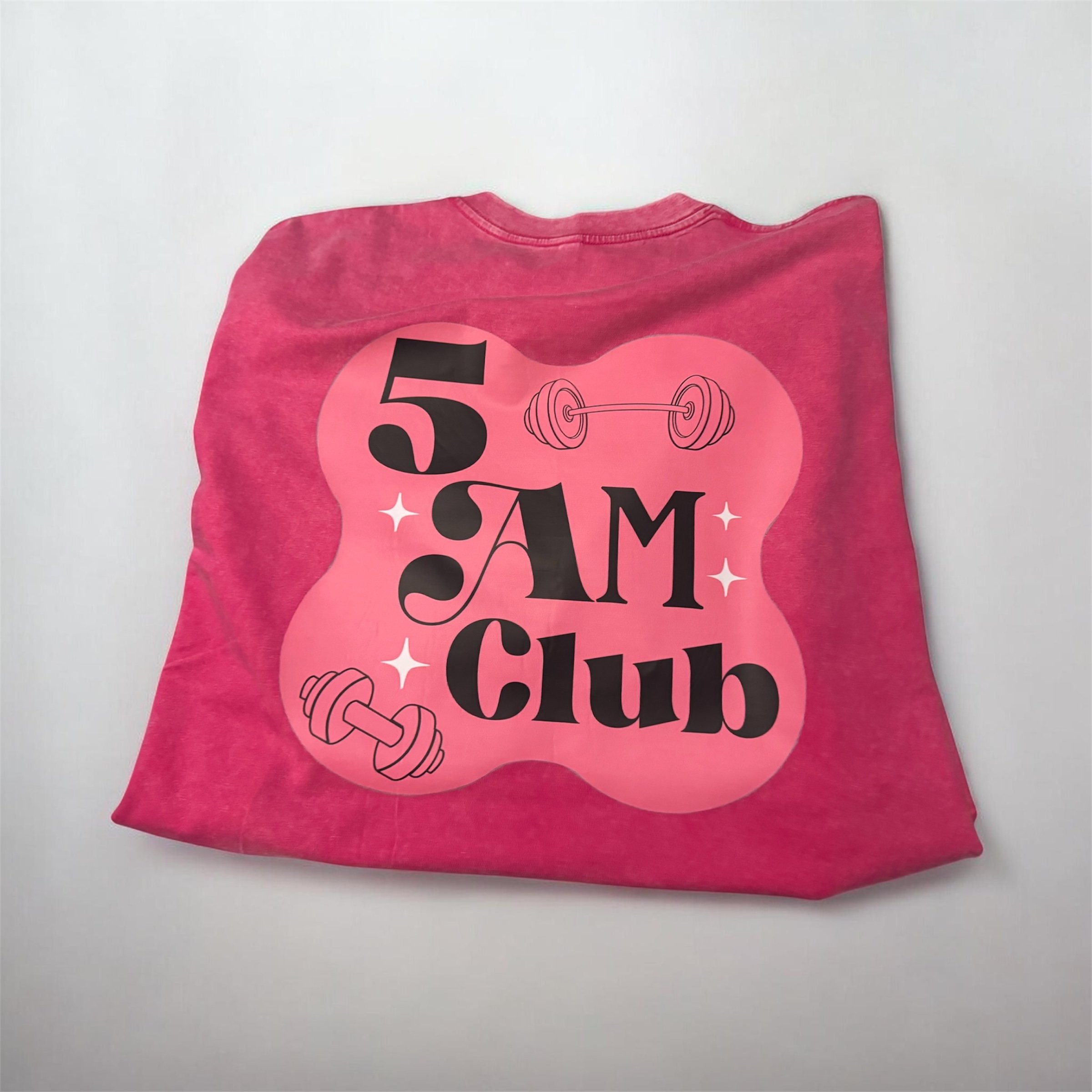 Pink T-shirt with a black and pink graphic text that says '5 AM Club' and includes a line drawing of a dumbbell.