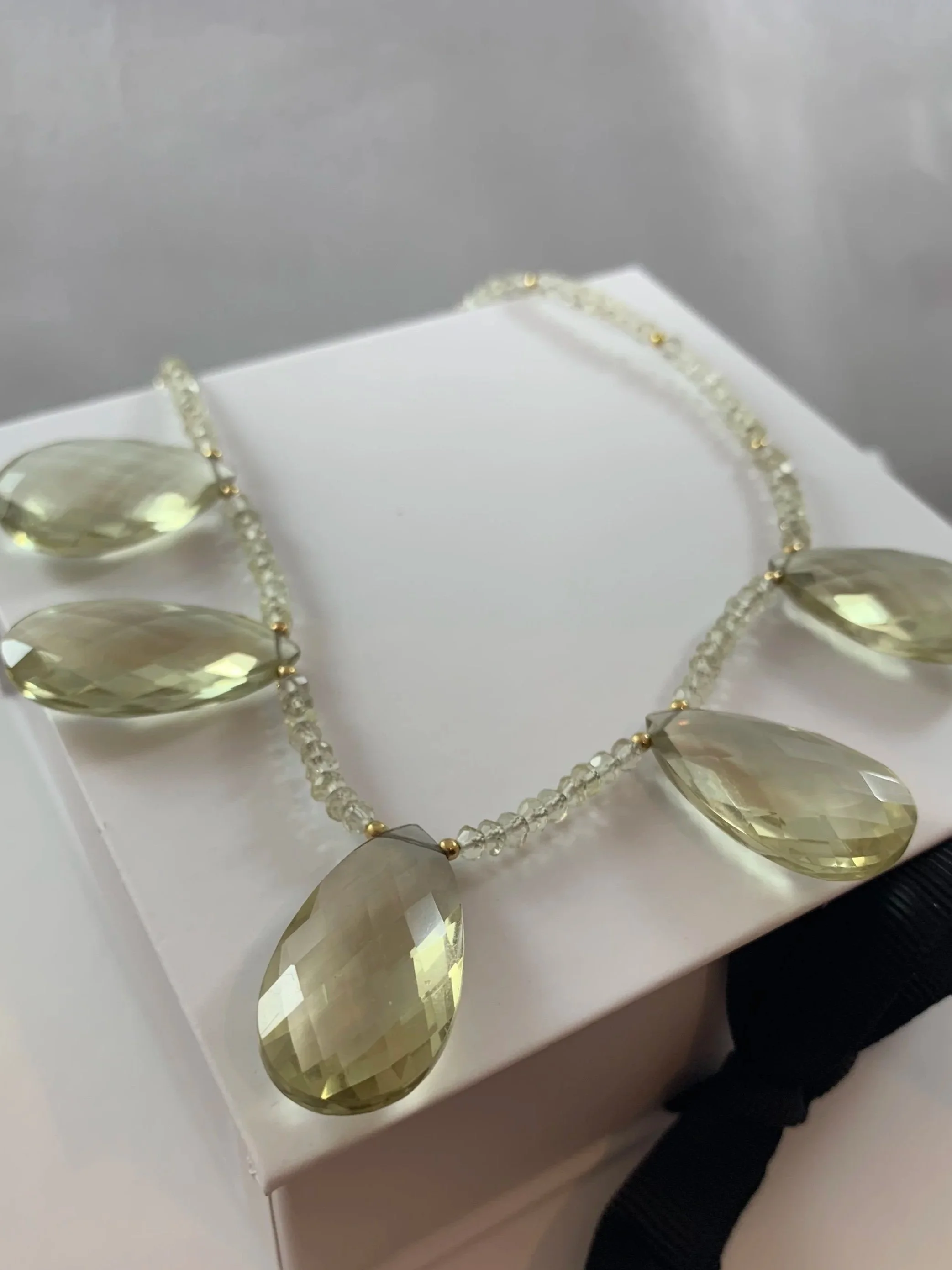 A jewelry necklace with large, faceted, pale yellow teardrop-shaped beads on a white display box.