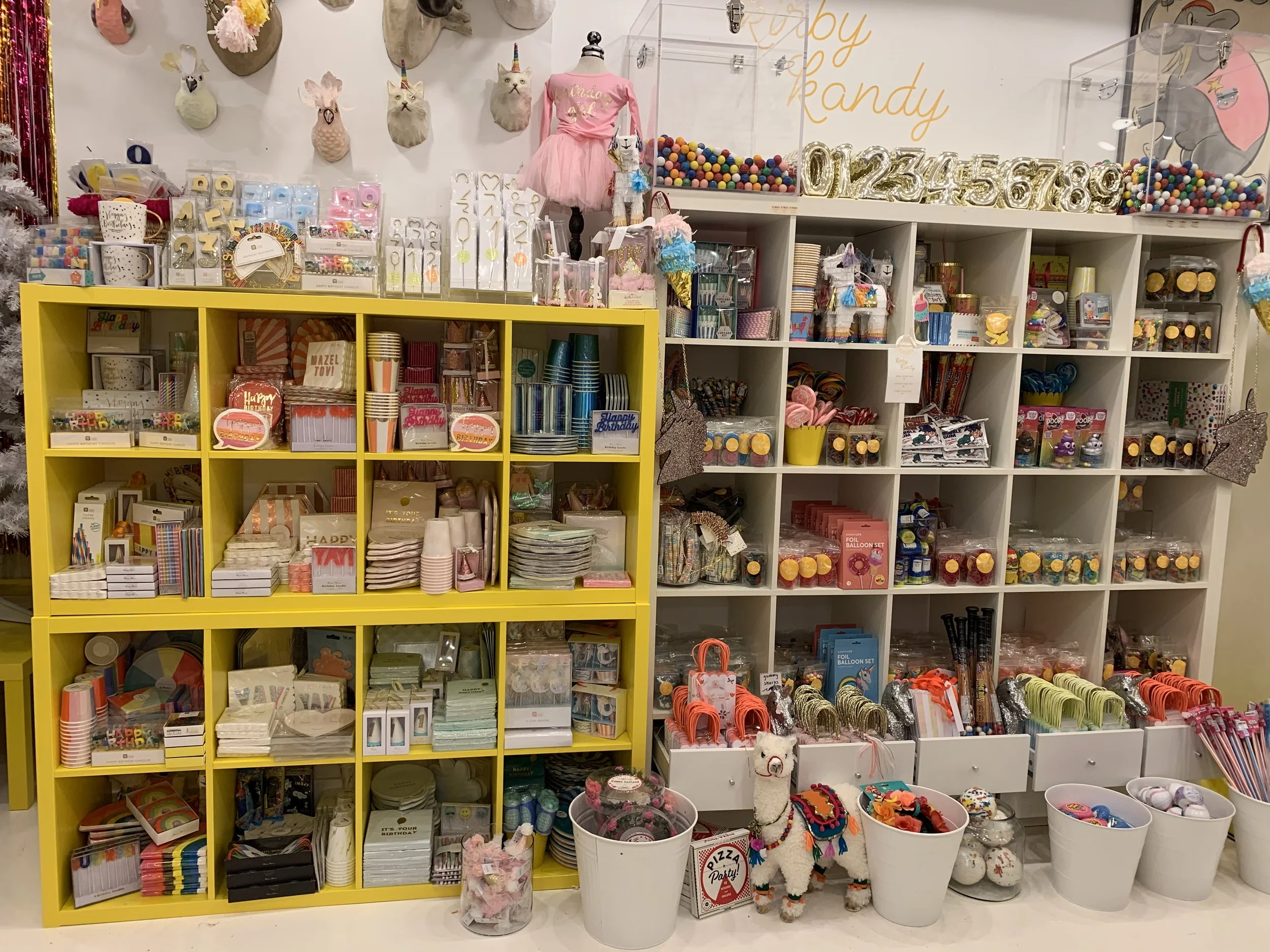 A display of party supplies and decorations, including cake toppers, balloons, cups, plates, ribbons, and unicorn-themed items in a store.